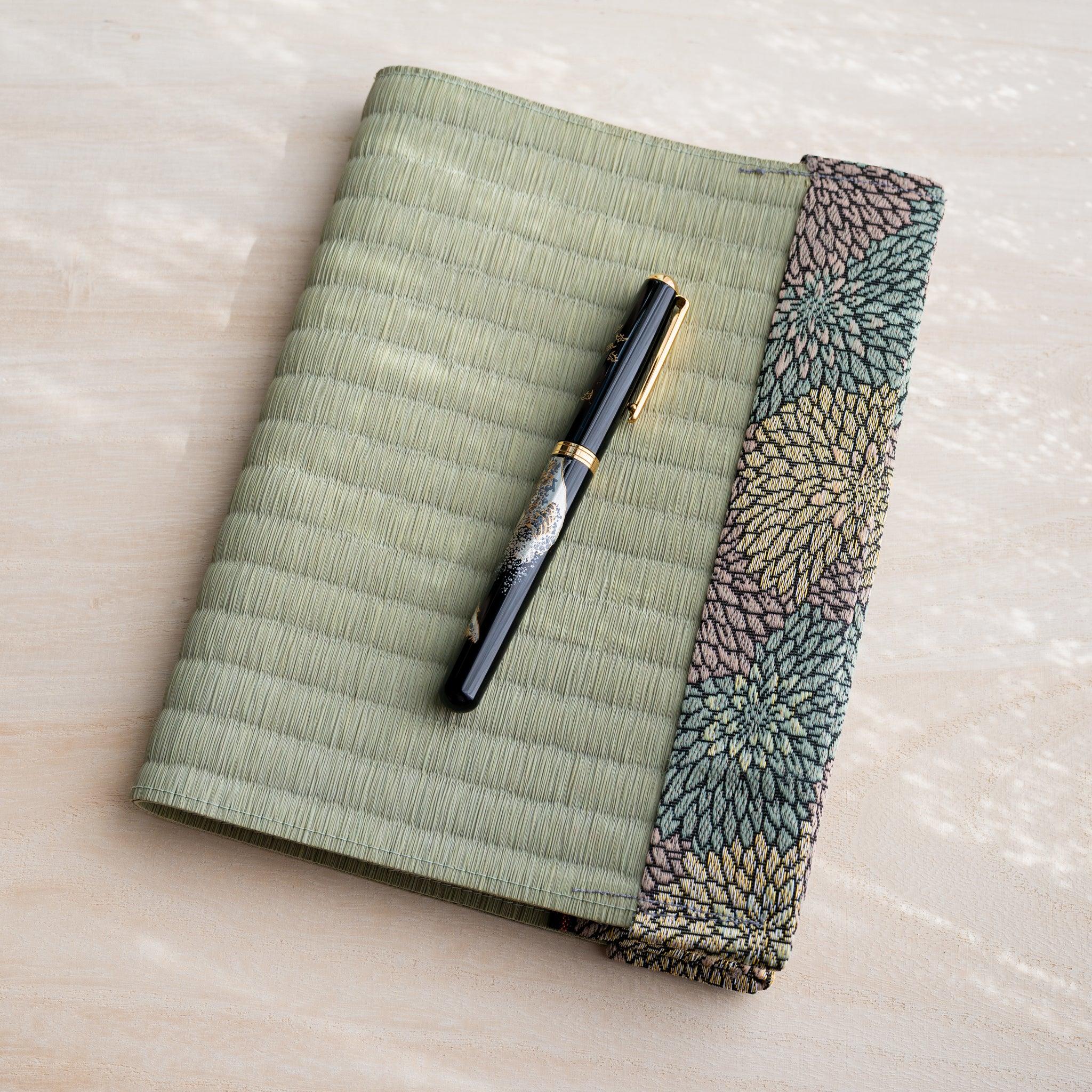 Black and gold fountain pen resting on closed tatami book cover with green pink and yellow chrysanthemum fabric band