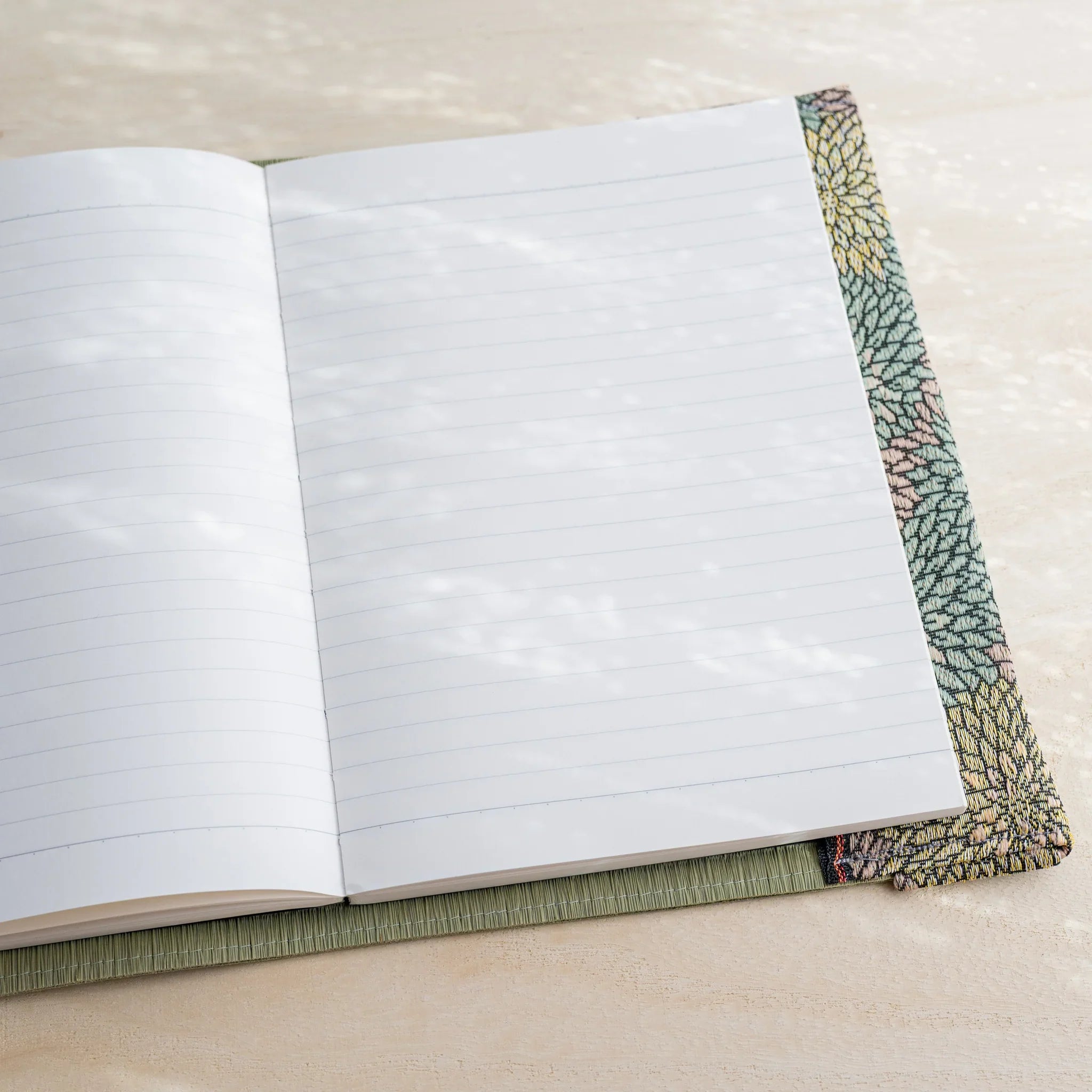 Angled view of tatami book cover open to white lined notebook pages with chrysanthemum patterned fabric edge