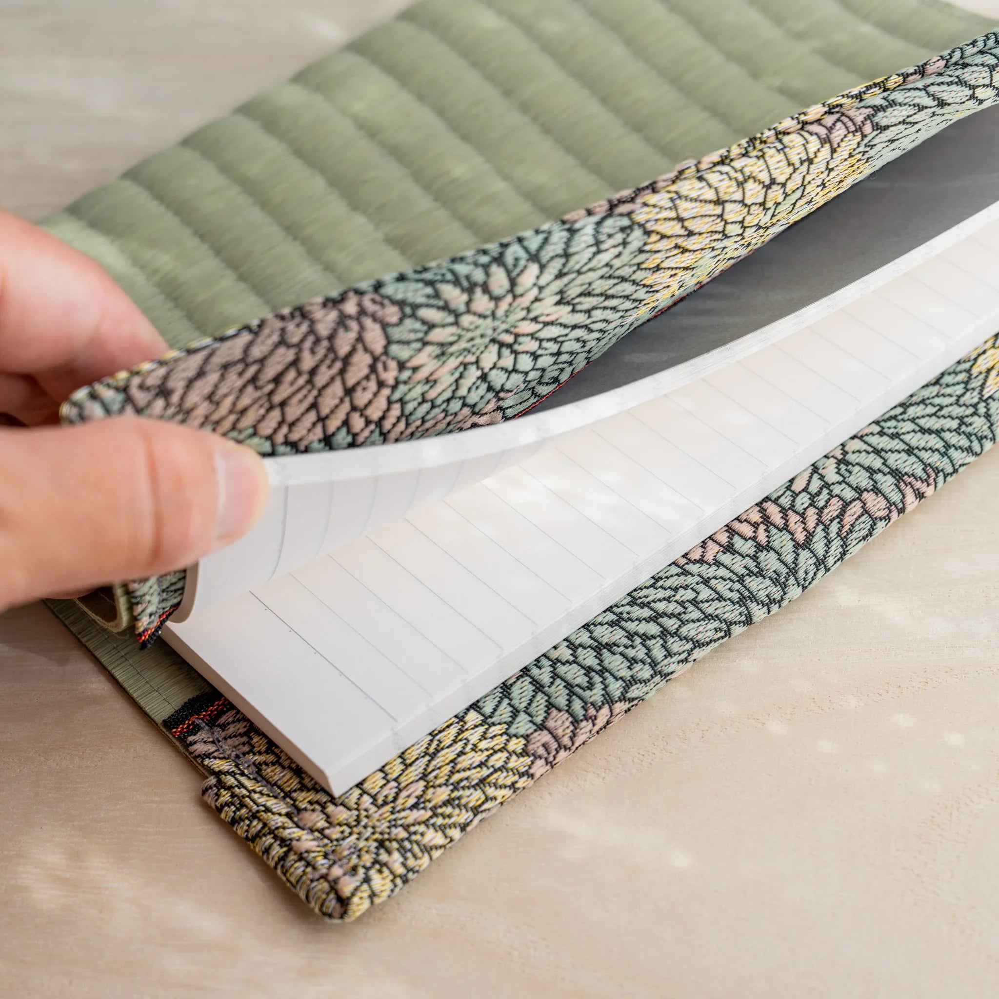 Hand lifting the Elegant Chrysanthemum tatami book cover flap to show the white lined notebook pages held inside