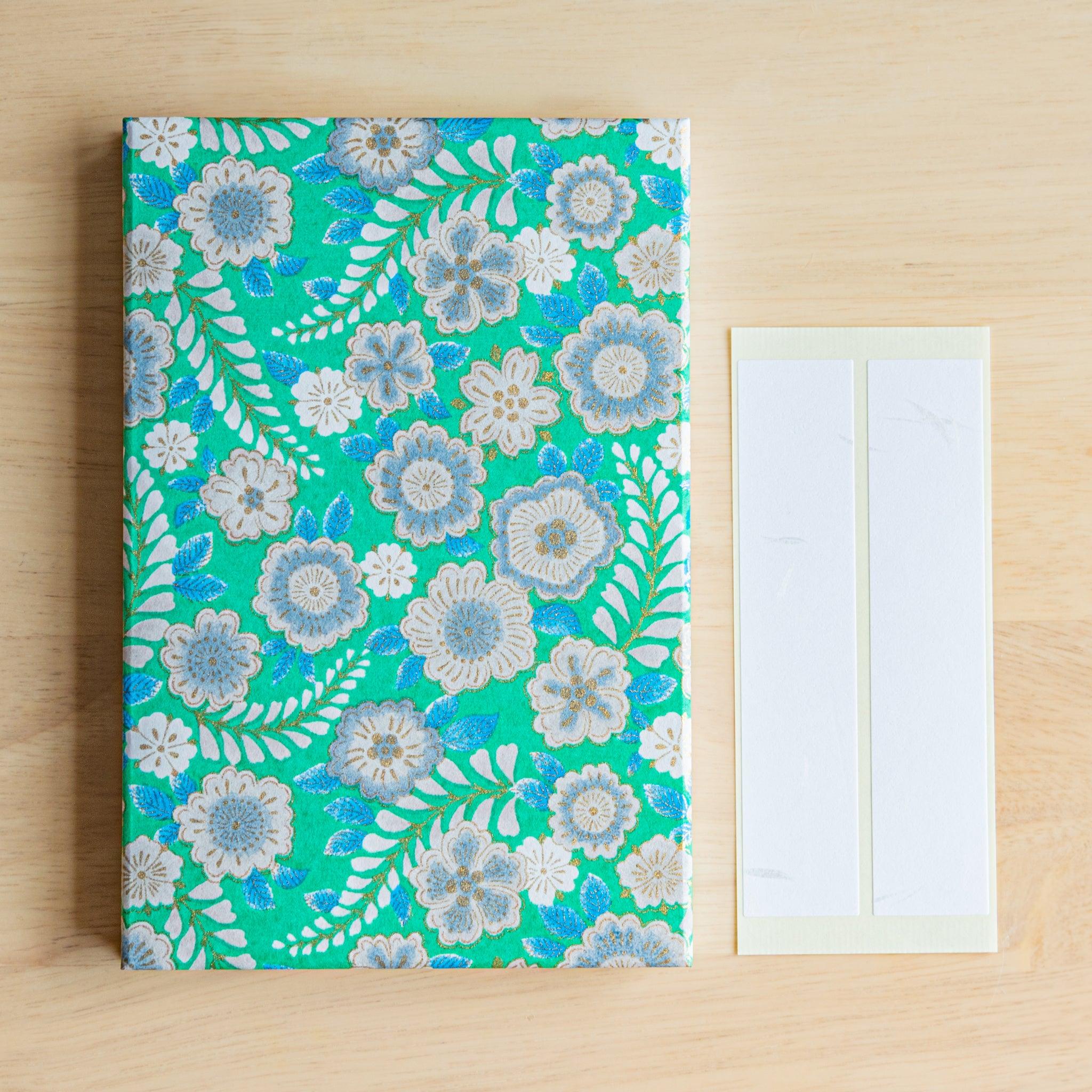 Close-up of emerald green Goshuincho Japanese stamp book with delicate washi paper, floral motifs, and included labels.