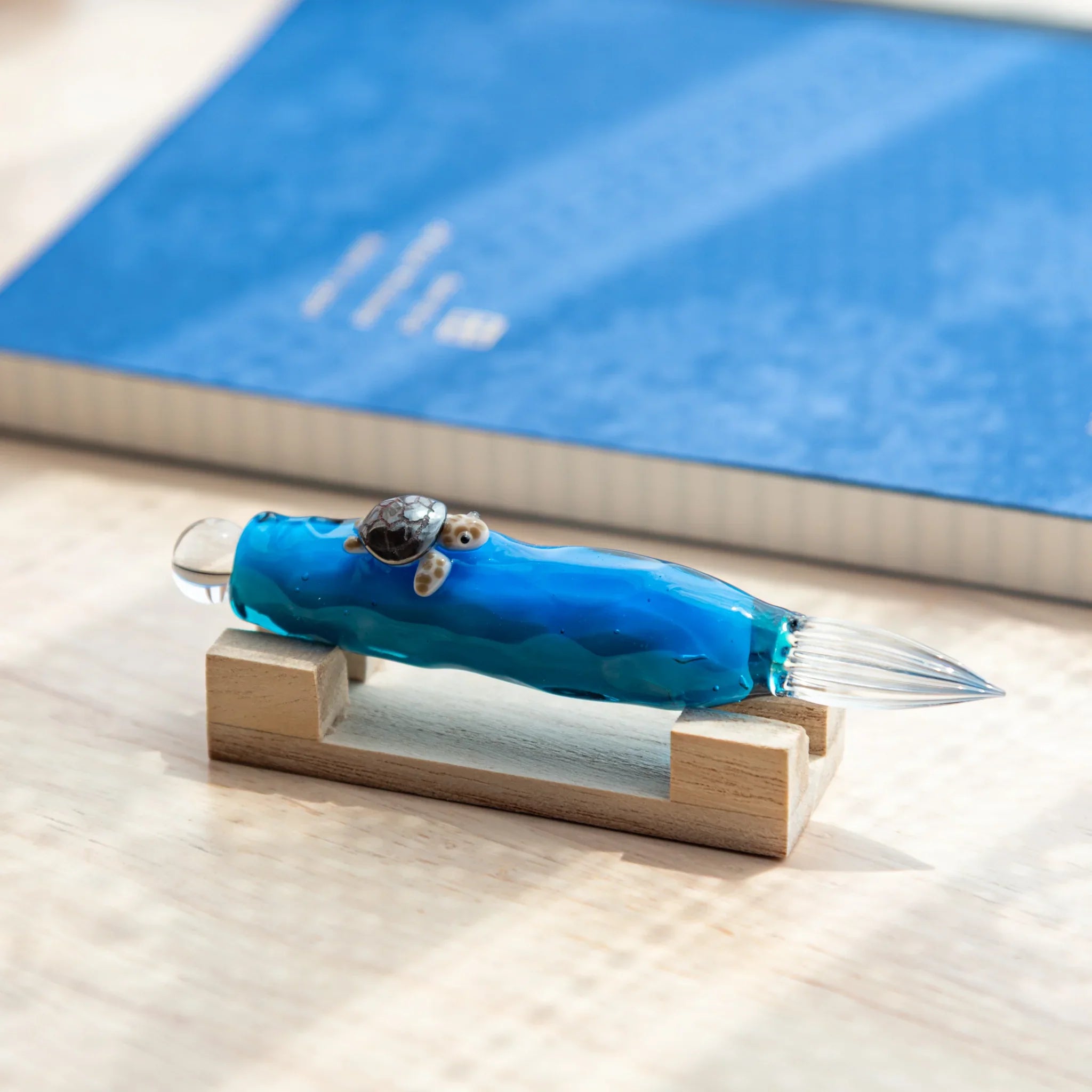 Floating Sea Turtle Japanese Glass Dip Pen resting on wooden stand, showcasing blue ocean glass and turtle figure.
