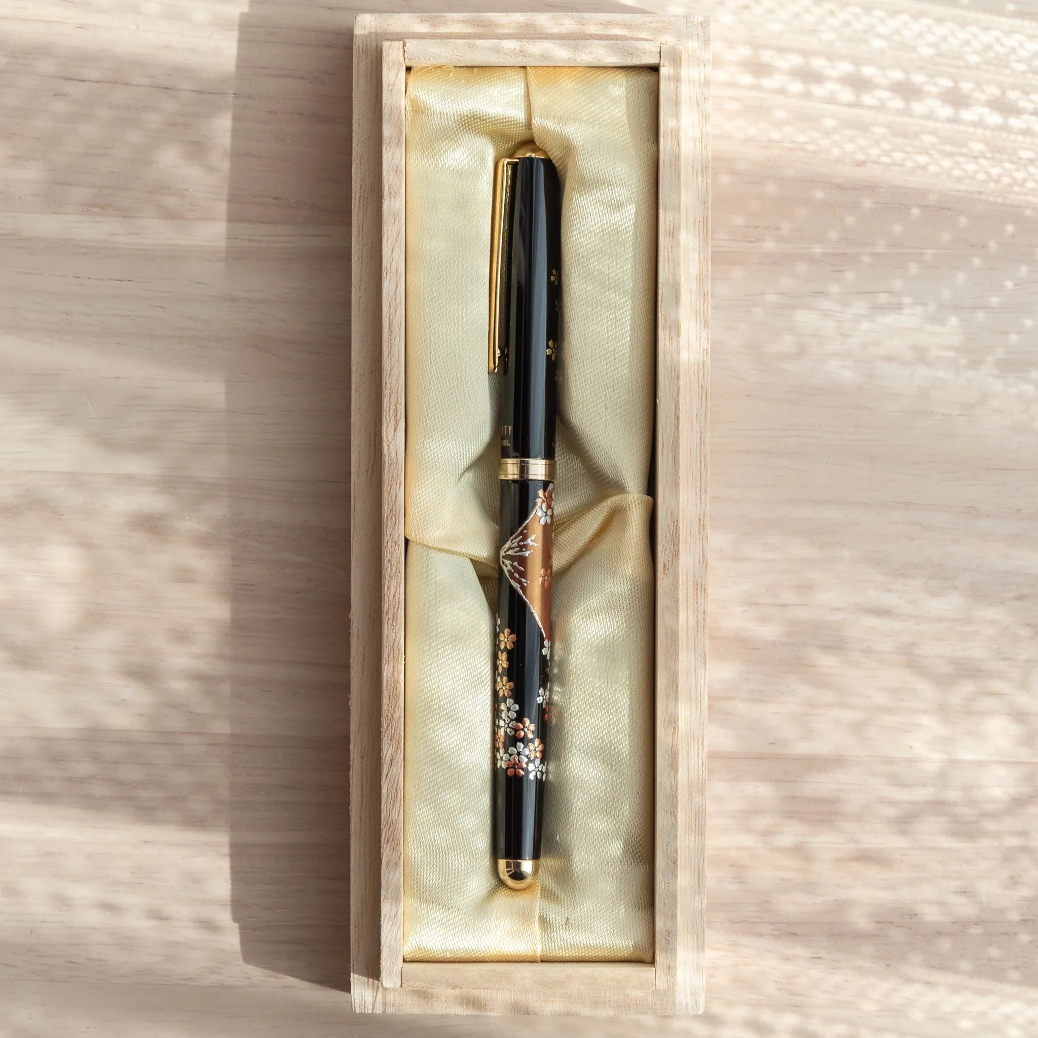 Japanese Ballpoint Pen with Lacquer sakura and Mt. Fuji motif resting in a golden-lined wooden box.