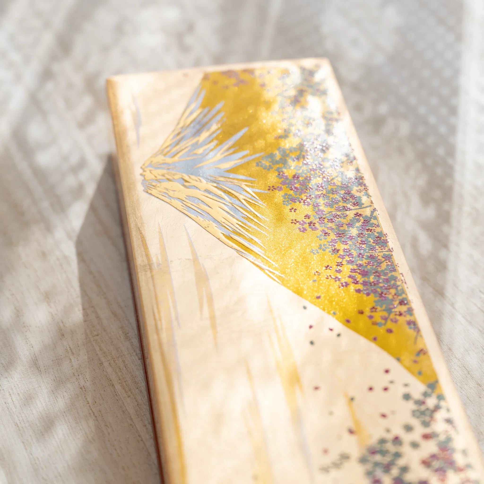 Close-up of a Japanese pen case lid with gold and silver mt. fuji motif and cherry blossom accents