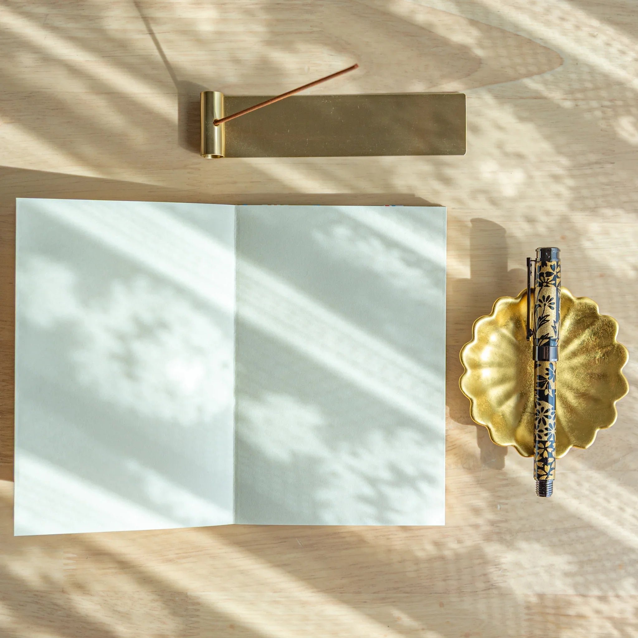 Japanese goshuincho stamp book open to blank pages on sunlit wood desk, with brass incense holder and patterned fountain pen