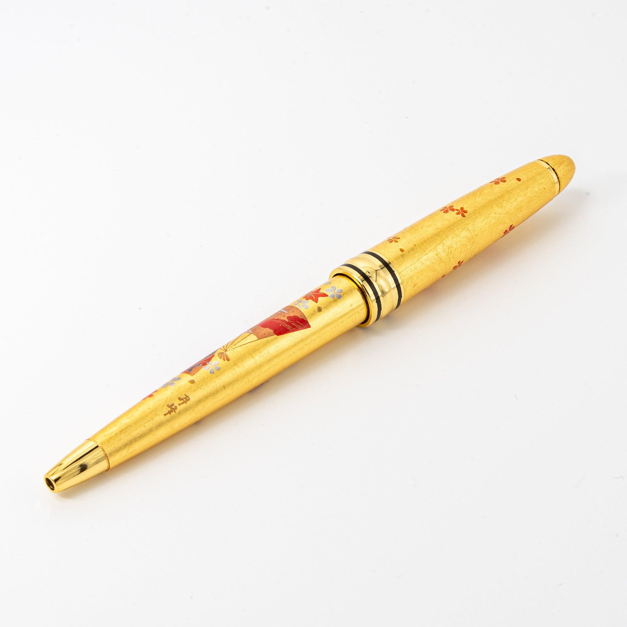The gold maki-e ballpoint pen displayed on a white background, highlighting its elegant floral and fan patterns.