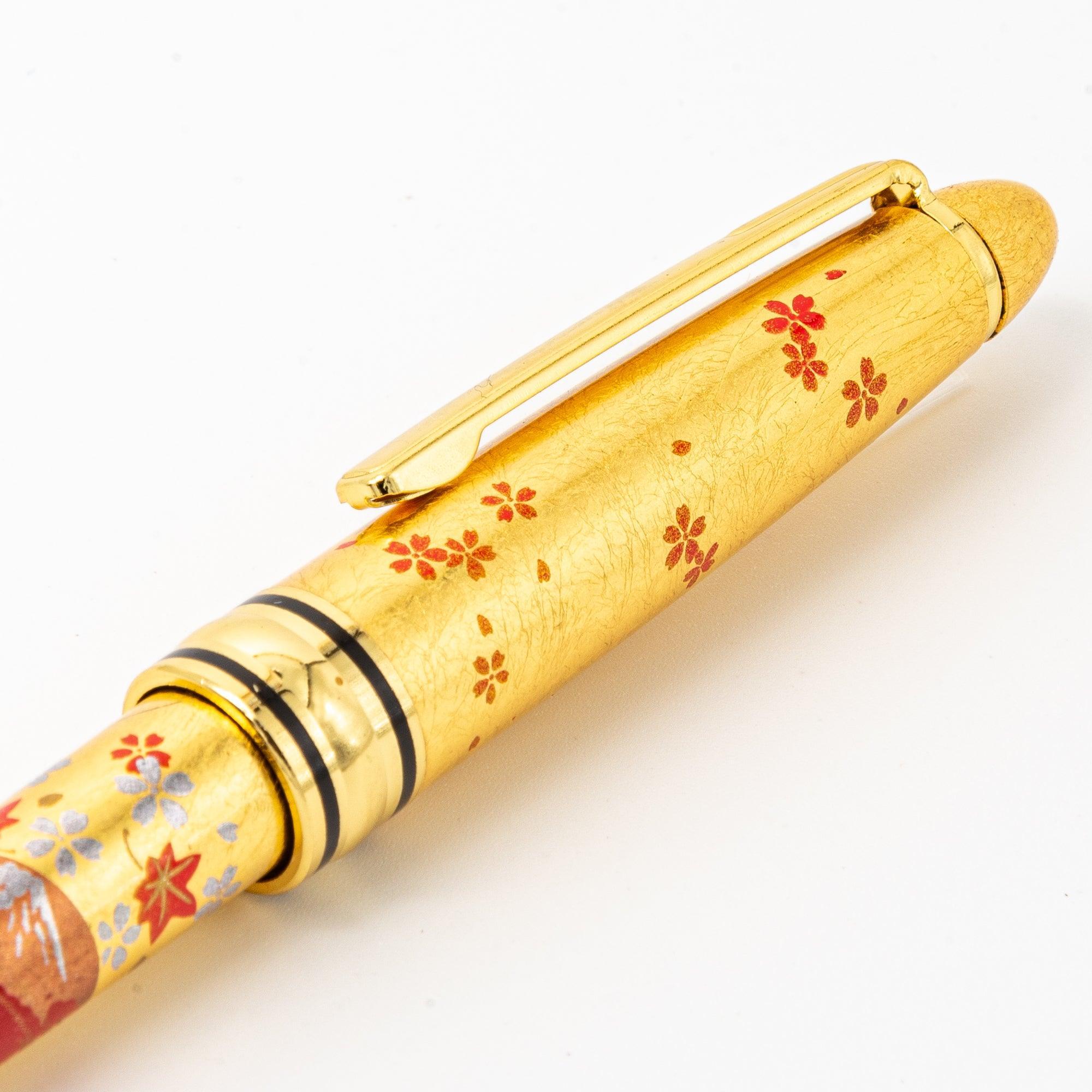 A gold ballpoint pen with Japanese makie lacquerwork featuring delicate cherry blossoms, fans, and scenic motifs, elegantly designed for writing enthusiasts.