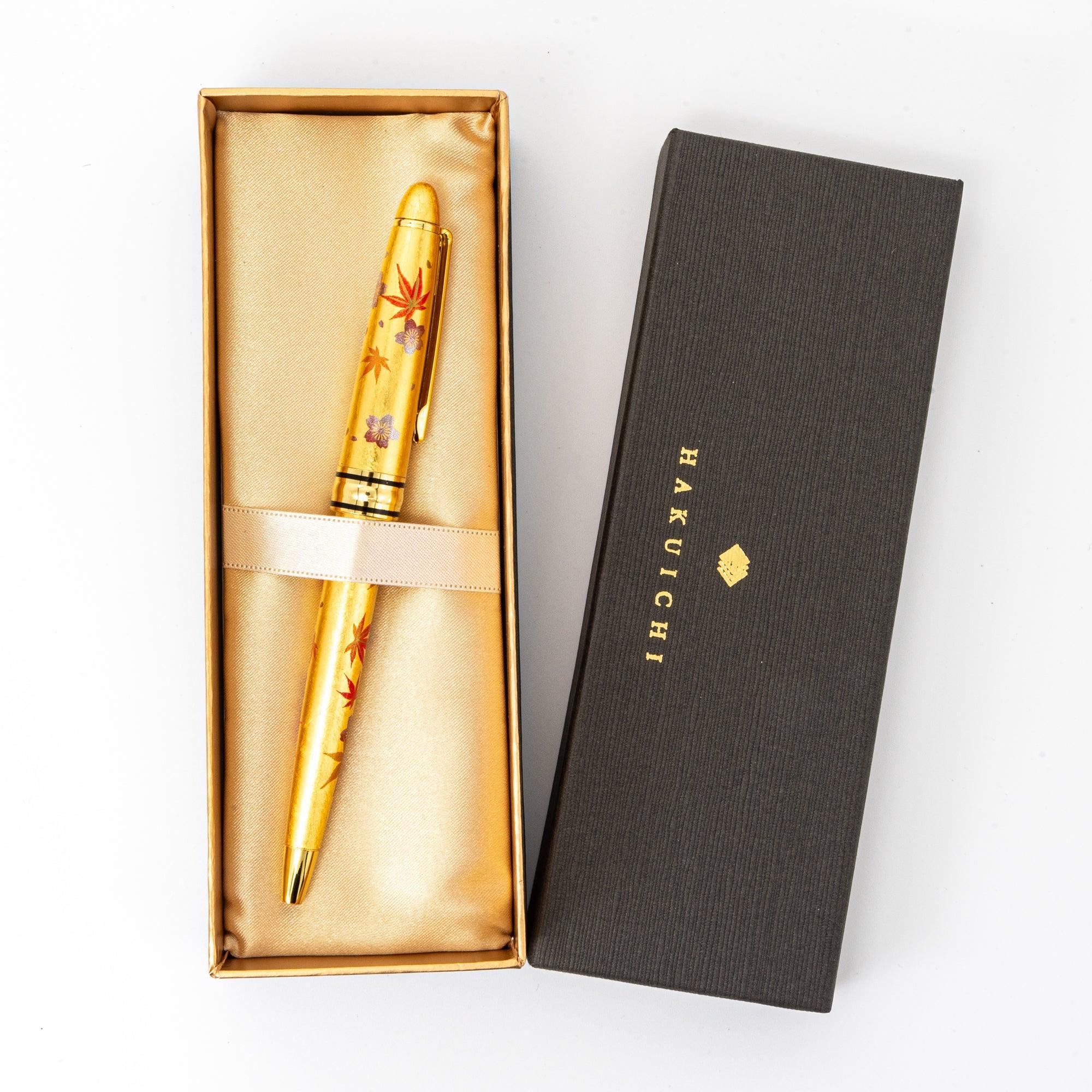 A gold ballpoint pen with sakura and momiji designs in a satin-lined box, presented elegantly with the Hakuichi logo on the lid.