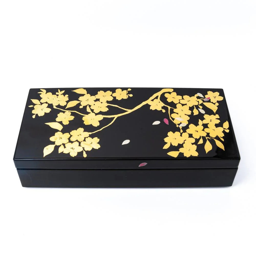 Black lacquer pen box at an angle, lid decorated with gold leaf sakura branch, flowers, and scattered pink and white petals