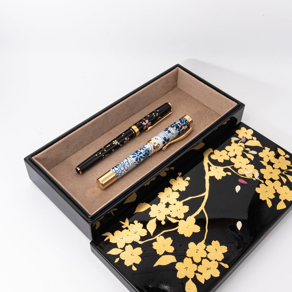 Open lacquer pen case with gold sakura design, displaying two pens with intricate patterns, emphasizing the craftsmanship of Japanese stationery.