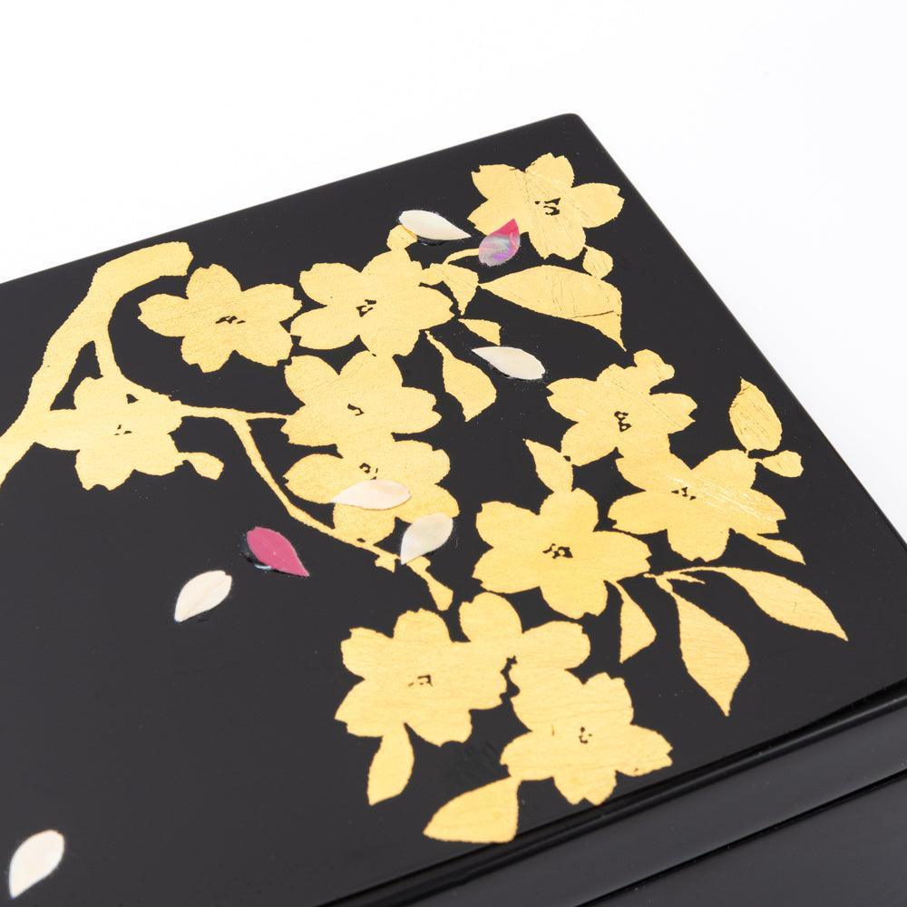 Close-up of a black lacquer pen case lid with golden sakura branches and scattered petals, showcasing the elegance of Japanese stationery.