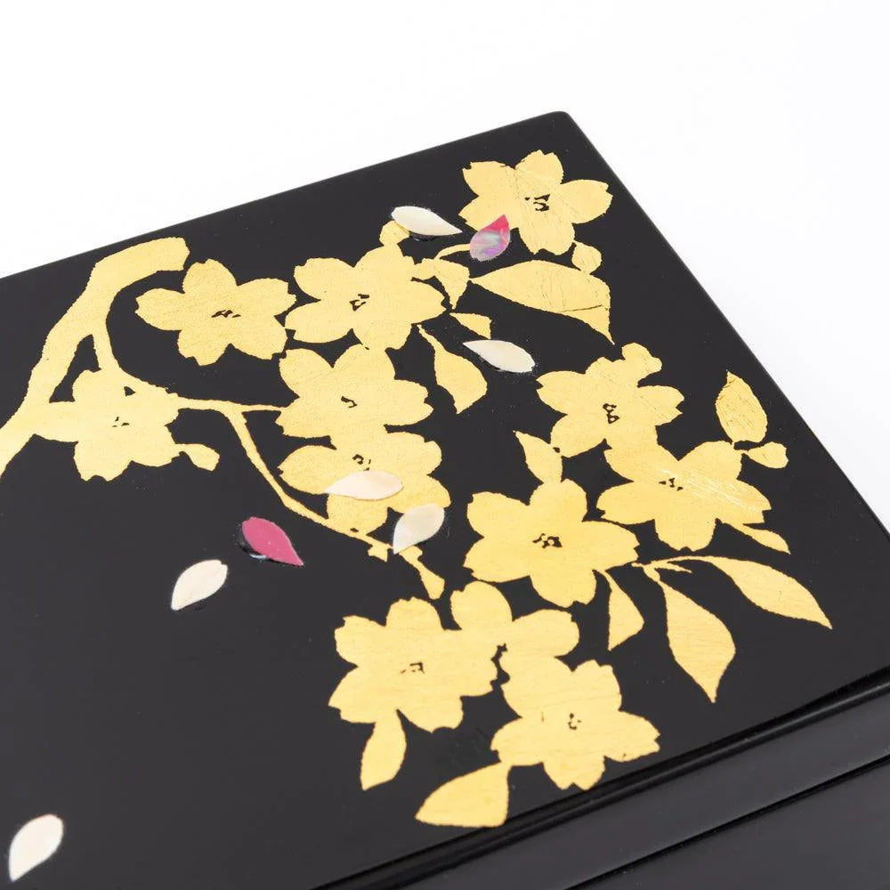 Close-up of black lacquer lid with gold leaf sakura flowers, pink and white petals scattered across the surface