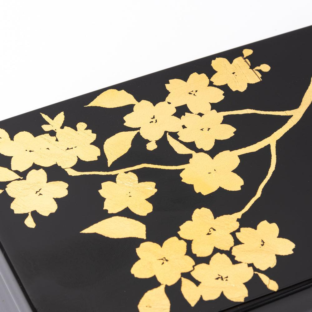 Detailed view of the golden sakura branch motif on a black lacquer pen case, emphasizing the exquisite craftsmanship of Japanese stationery.