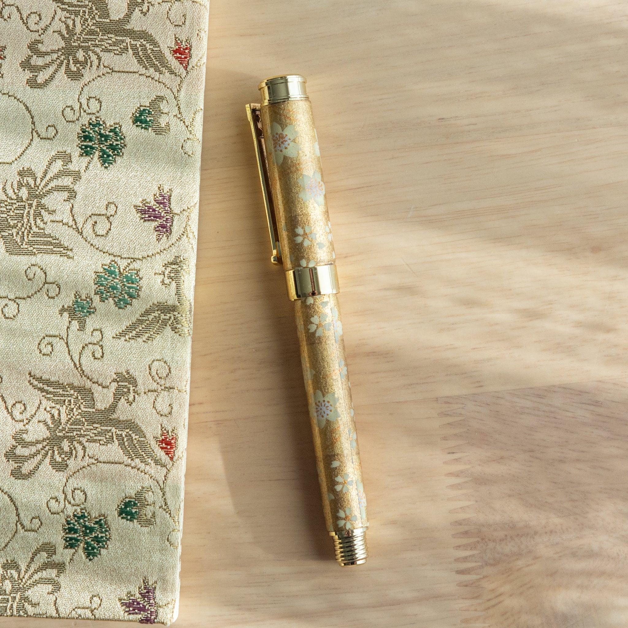 TACCIA fountain pen with cream Mino washi wrapper featuring small botanical flowers, gold accents, front angle view