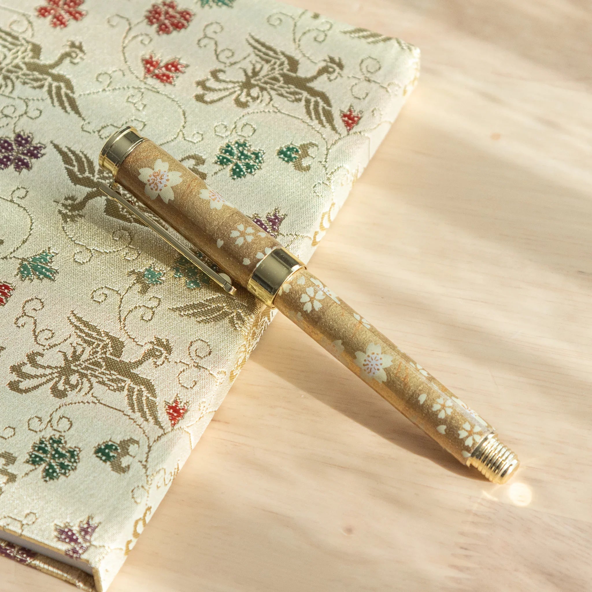 Gold Sakura Mino Washi fountain pen flat-lay on cream botanical fabric with delicate floral pattern and gold metallic accents