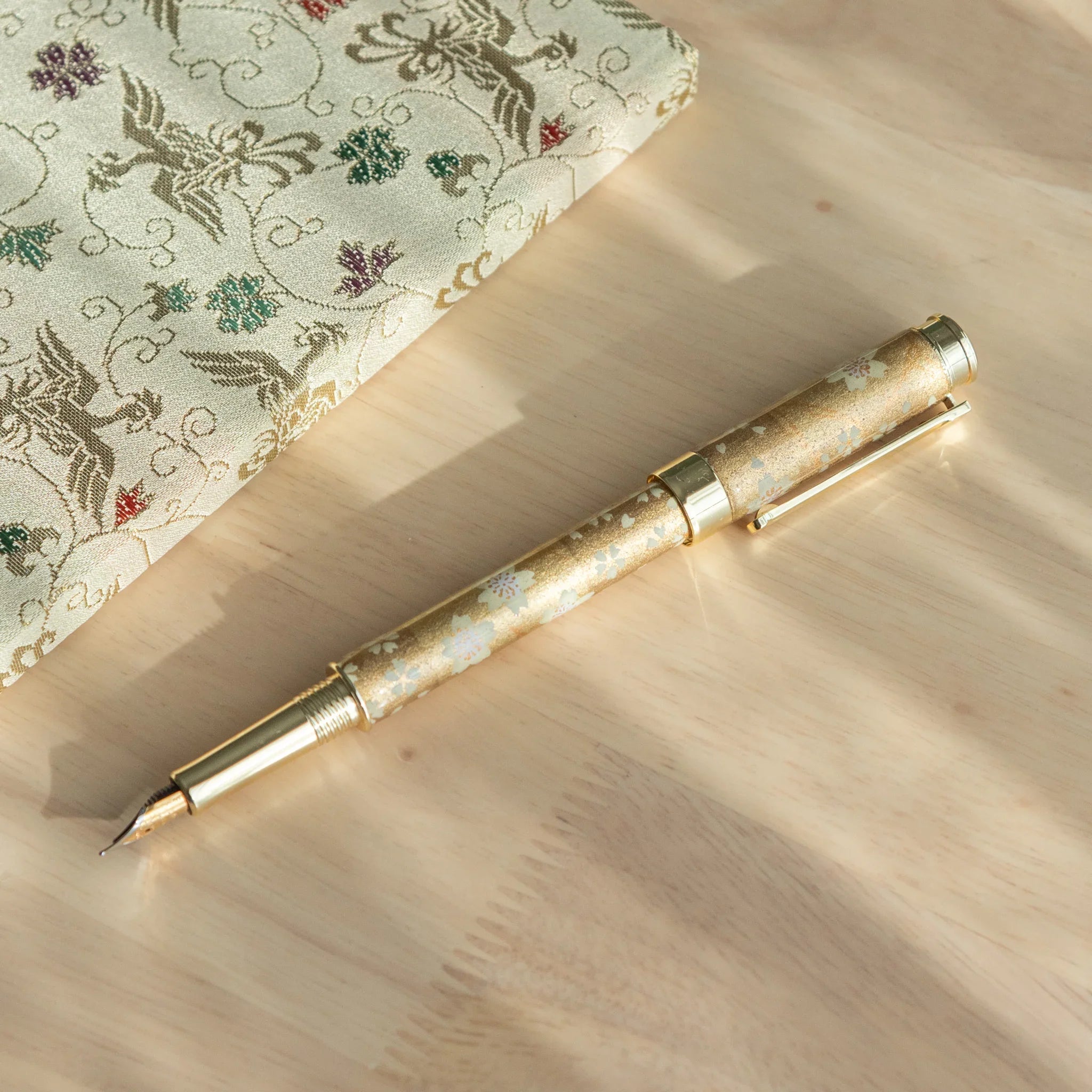 Gold Sakura Mino Washi fountain pen on cream fabric with botanical wrapper featuring gold sakura flower design accents