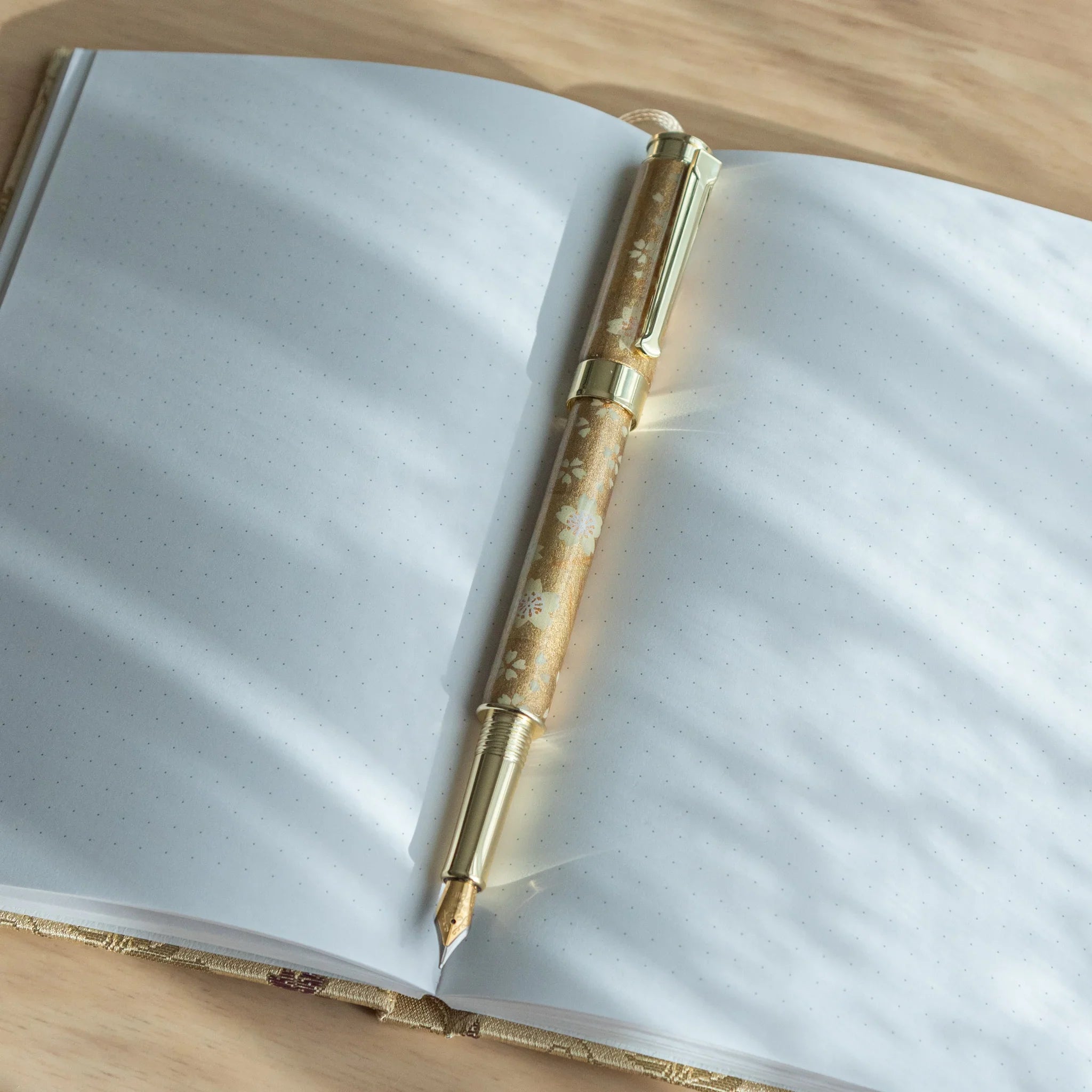Gold Sakura fountain pen barrel closeup highlighting delicate white flower blossoms with gold trim on cream Mino washi base