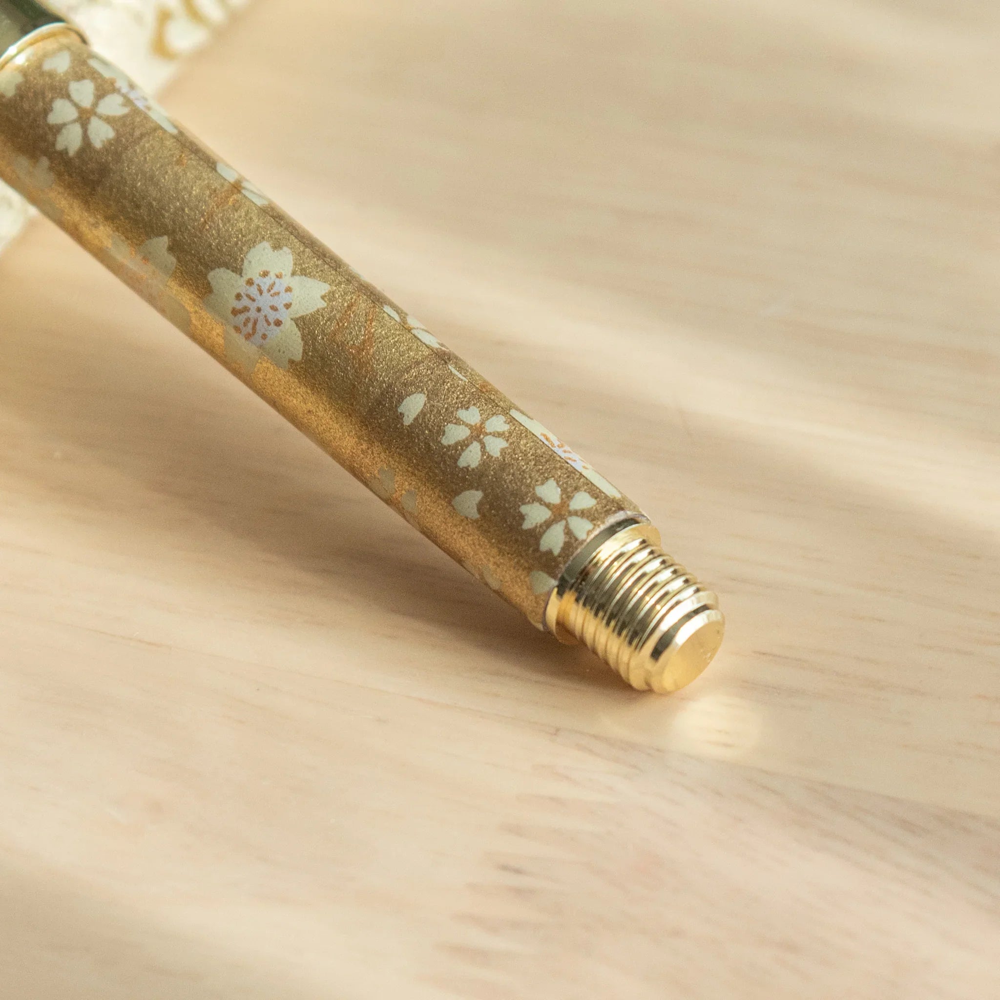 Gold Sakura Mino Washi fountain pen uncapped showing cream wrapper with botanical flower design and metallic gold accents