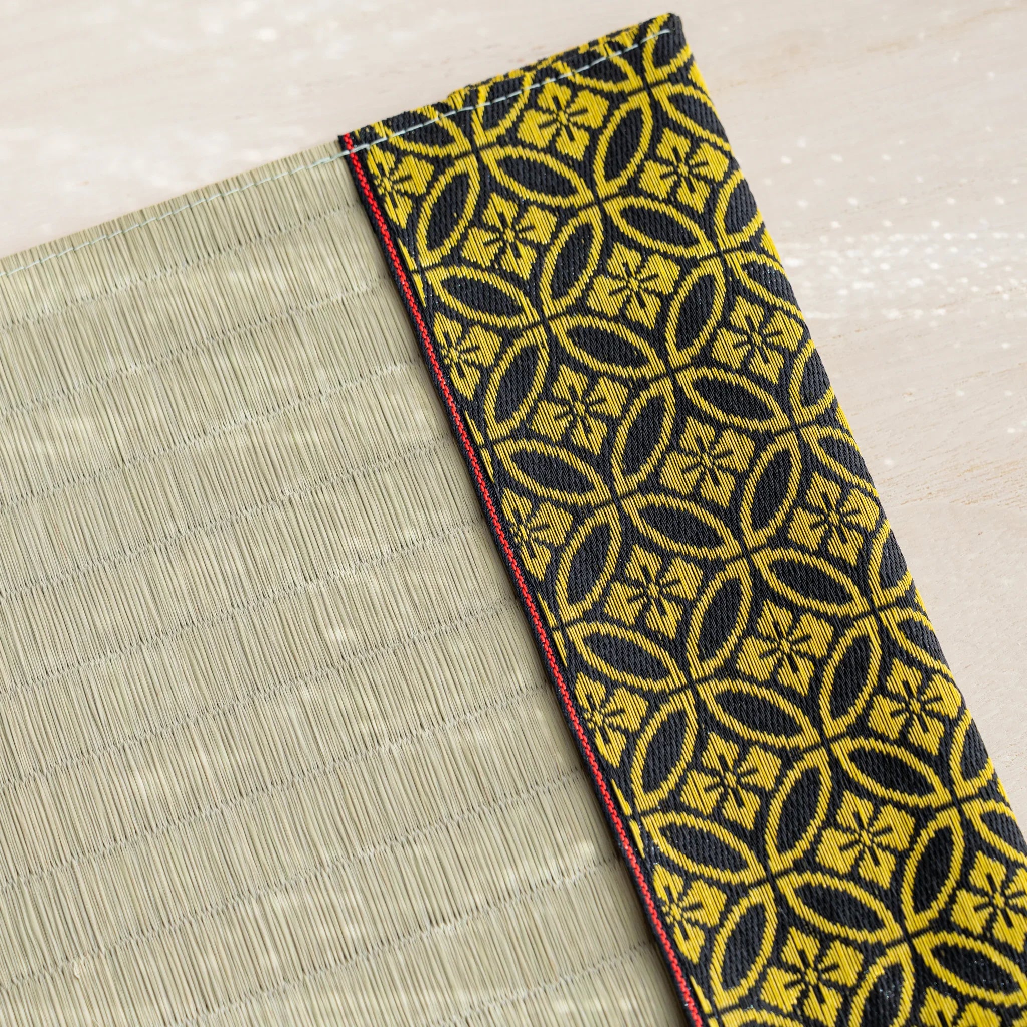Close-up of black and gold Japanese shippo interlocking circle brocade band with red stitched edge beside rush straw