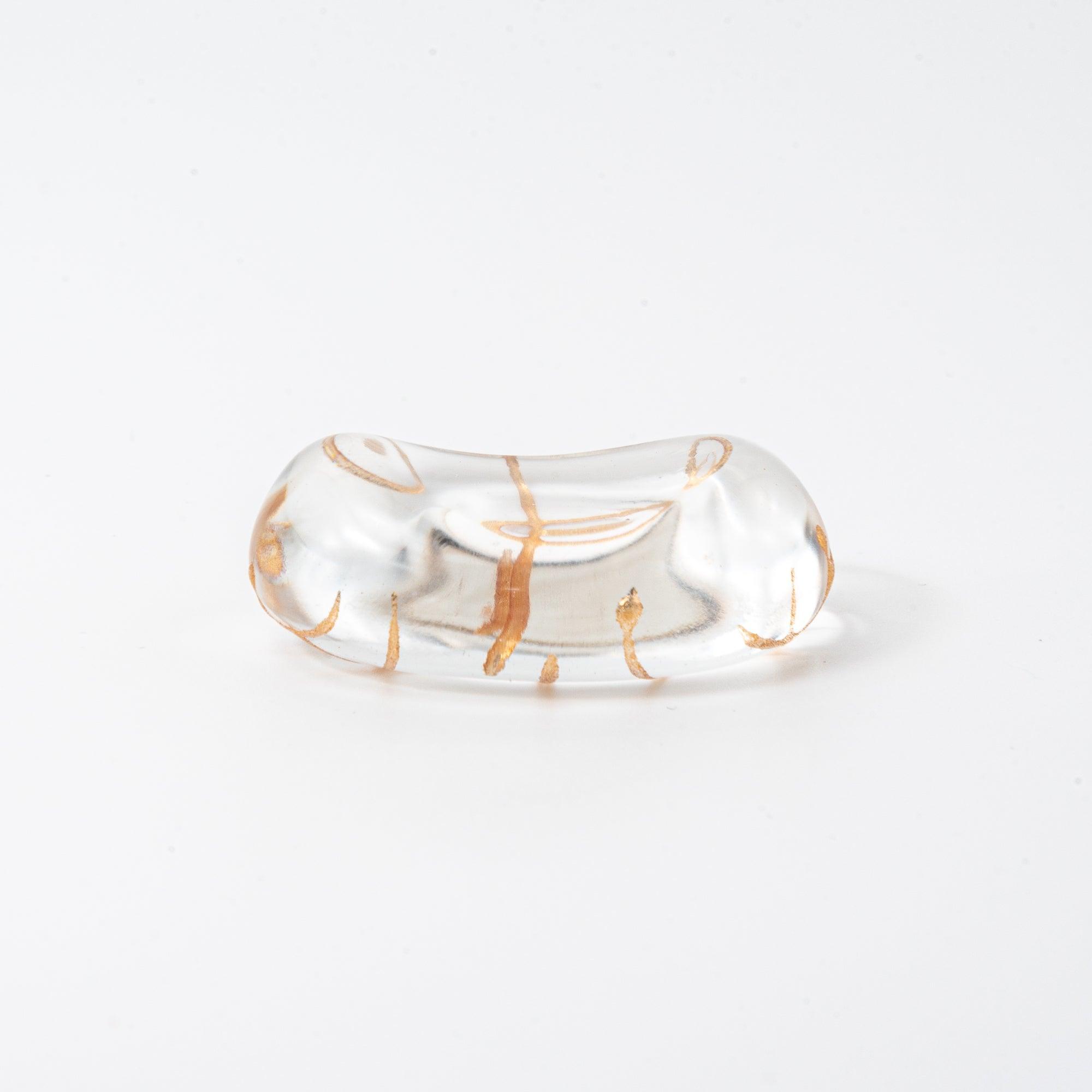 A clear oval-shaped glass pen rest with a gold-thread design, showcasing a simple yet elegant grid pattern.