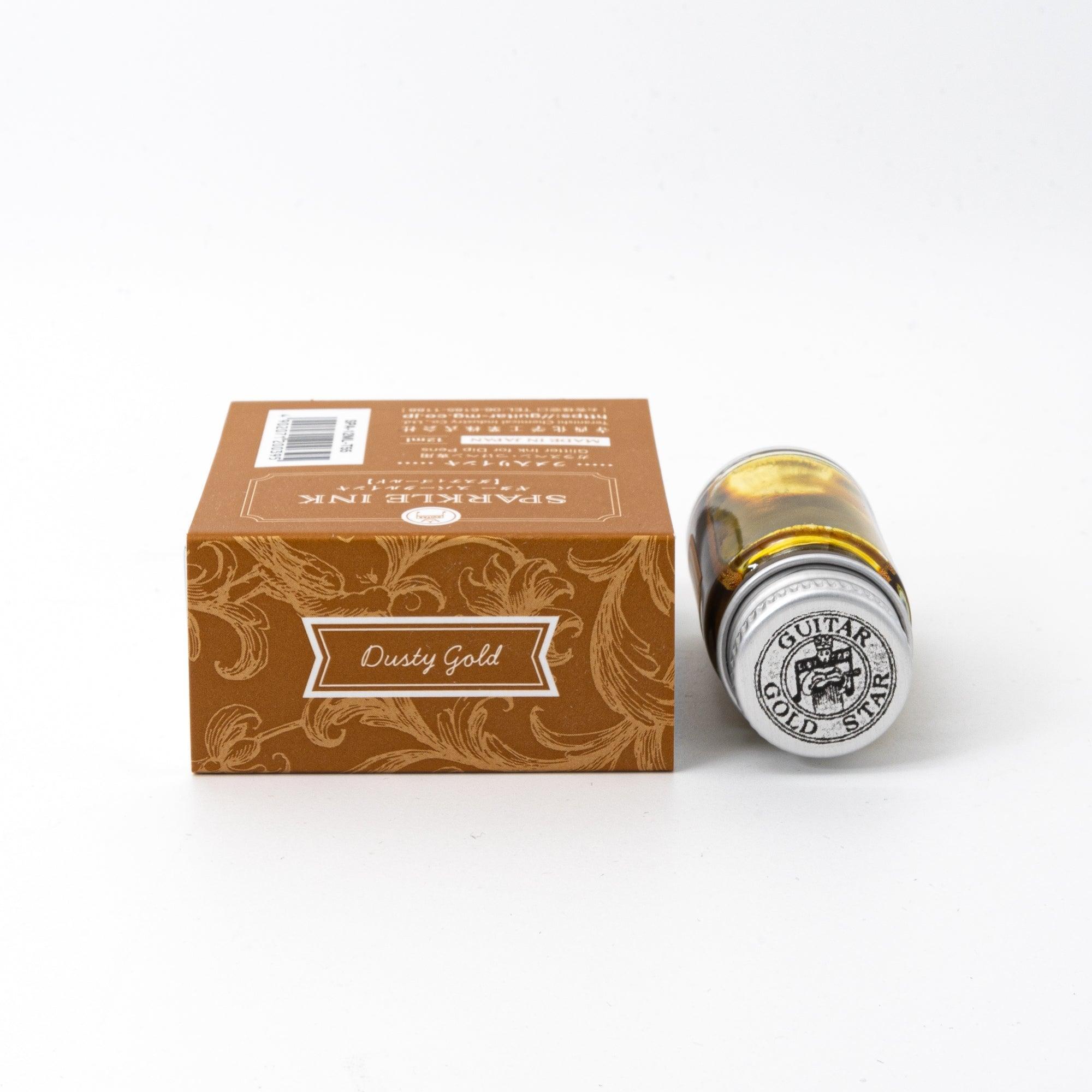 Sparkle Ink in Dusty Gold, packaged in a glass bottle paired with a golden box featuring intricate floral patterns and sophisticated typography.