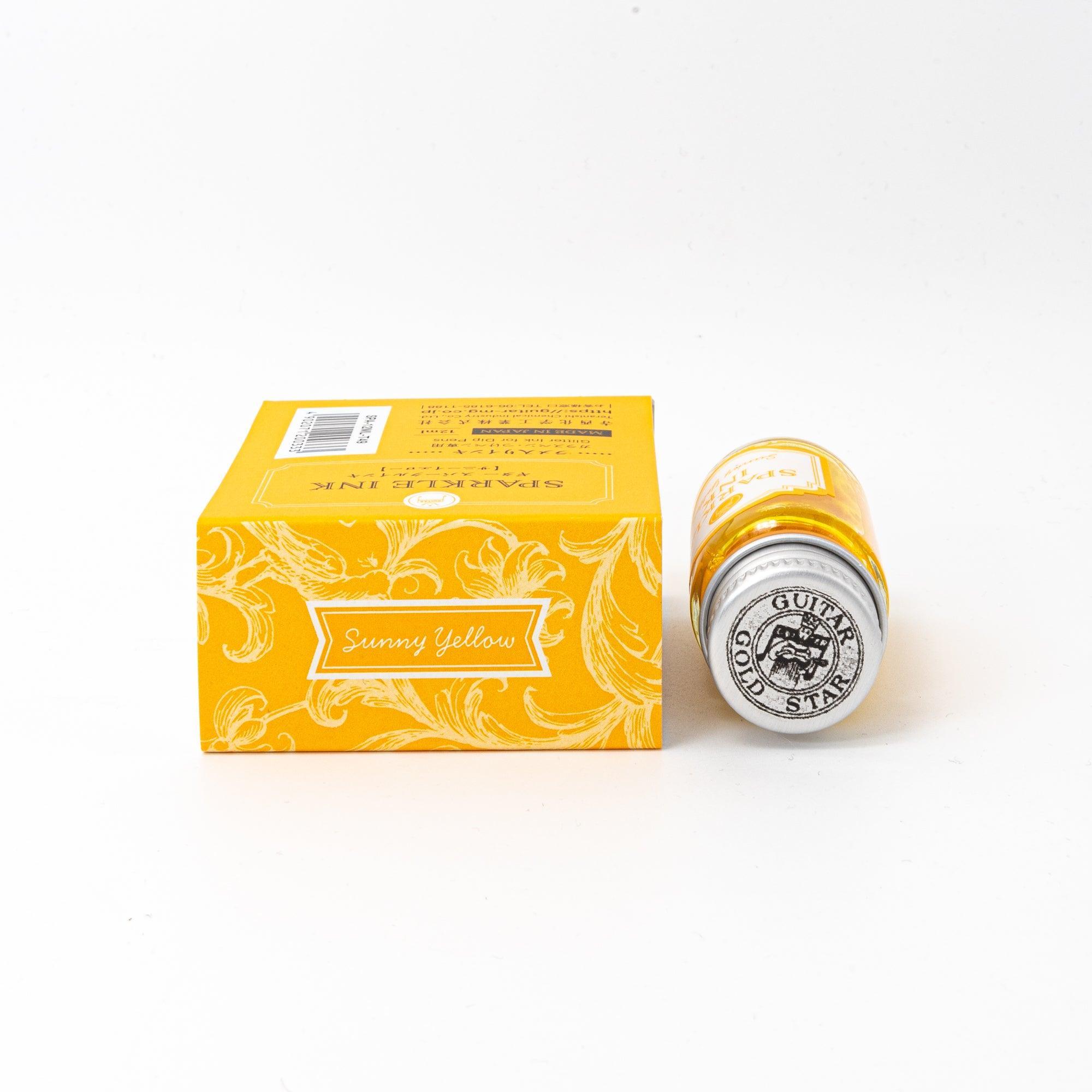 Sparkle Ink in Sunny Yellow, presented in a glass bottle with coordinating yellow packaging adorned with intricate floral designs and elegant text.