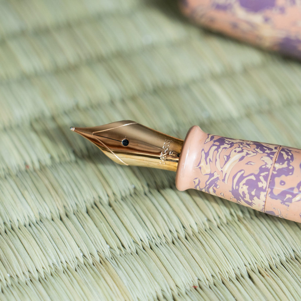 Macro of the Hanagasumi 14K gold nib stamped F, with pink section and pink and purple urushi barrel