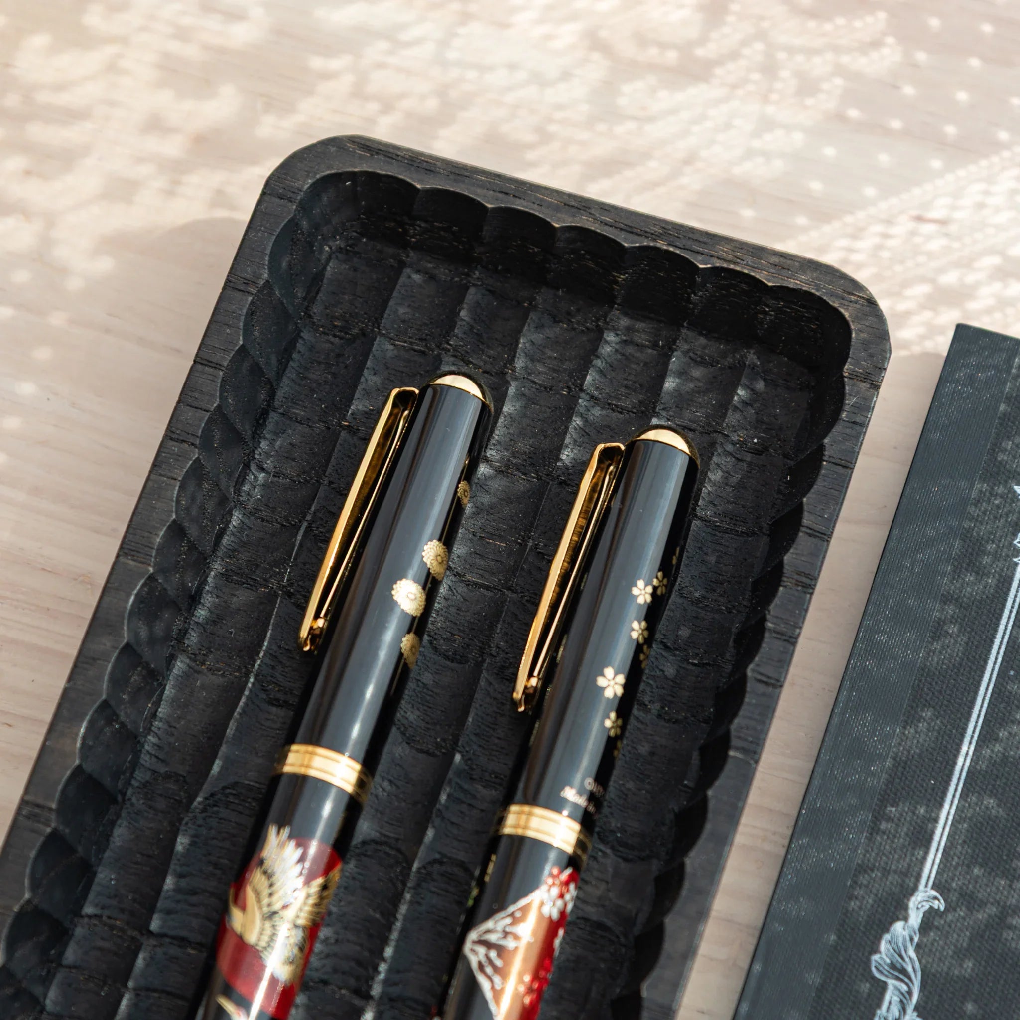 Two Japanese Fountain Pens displayed in a black hand-carved Japanese Pen Tray with parallel grooves.