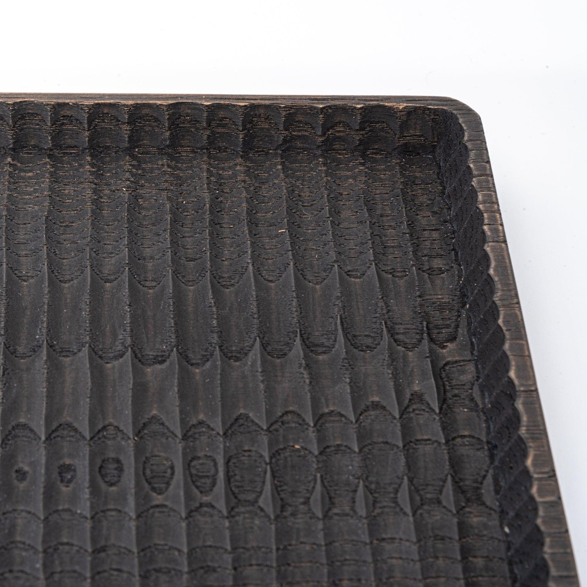 Close-up of a black wooden tray corner, highlighting its textured grooves and detailed edge.