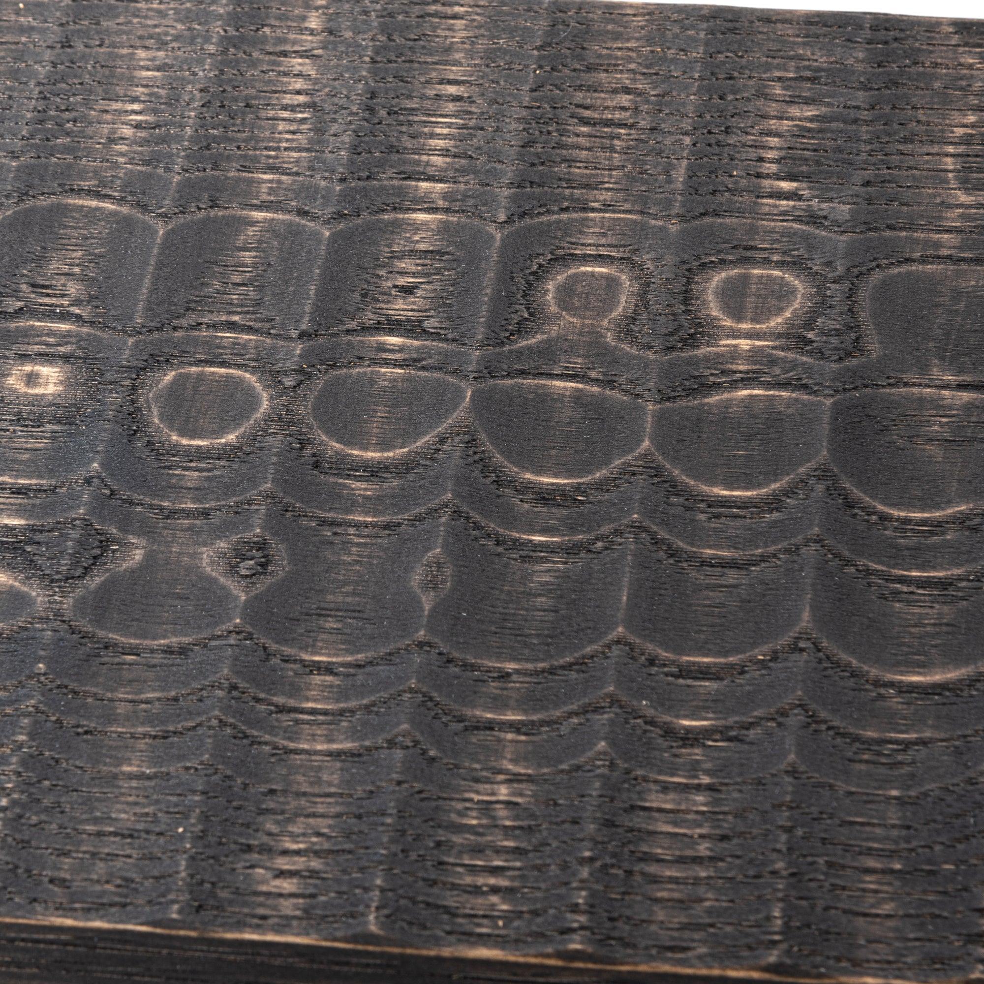 Close-up of a black wooden board highlighting detailed carved grooves and natural texture.