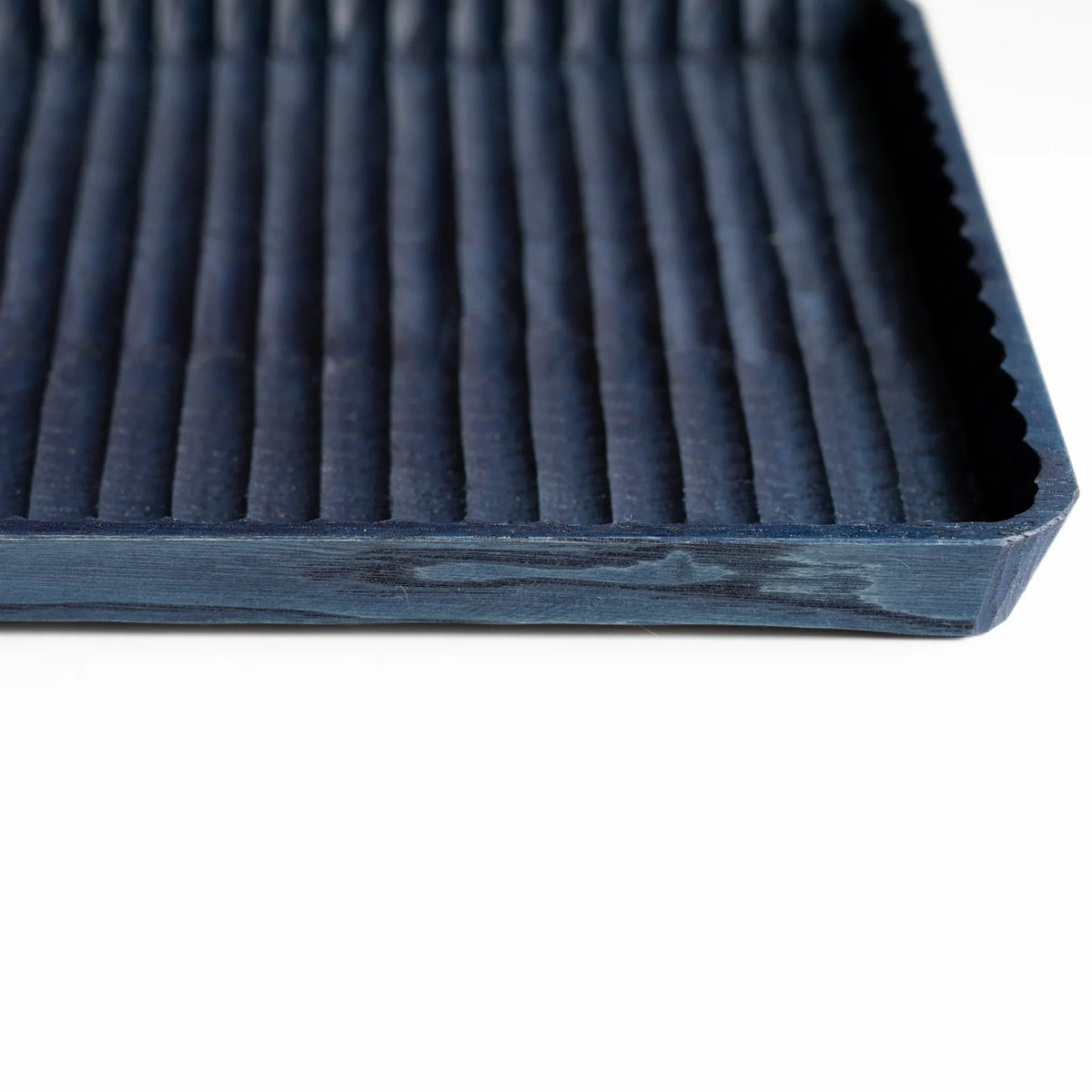 Angled view of indigo dyed chestnut pen tray showing carved grooves, scalloped rim and the thickness of the side