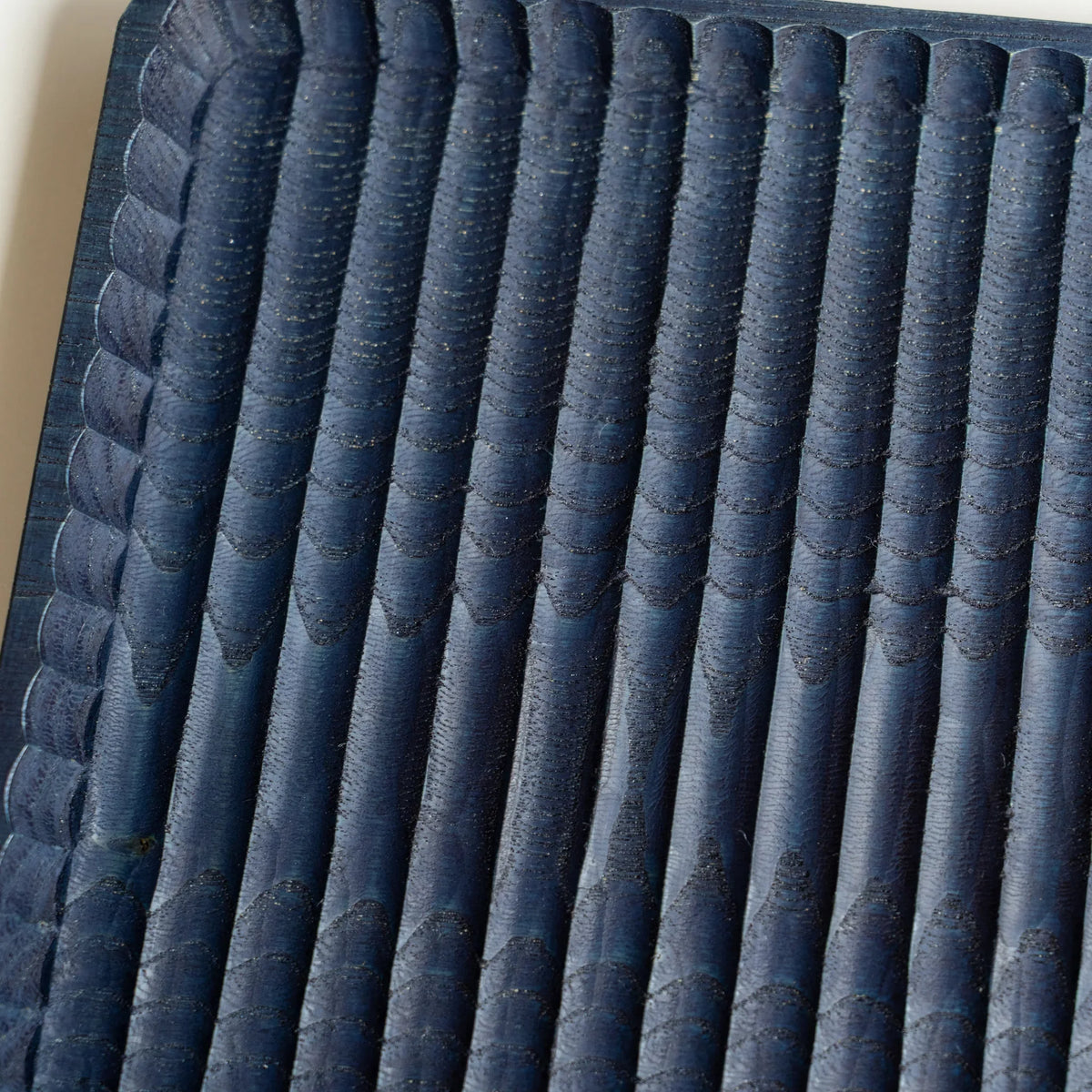 Close-up of indigo dyed chestnut showing chisel marks along the carved ridges, with paler blue on the ridge tops