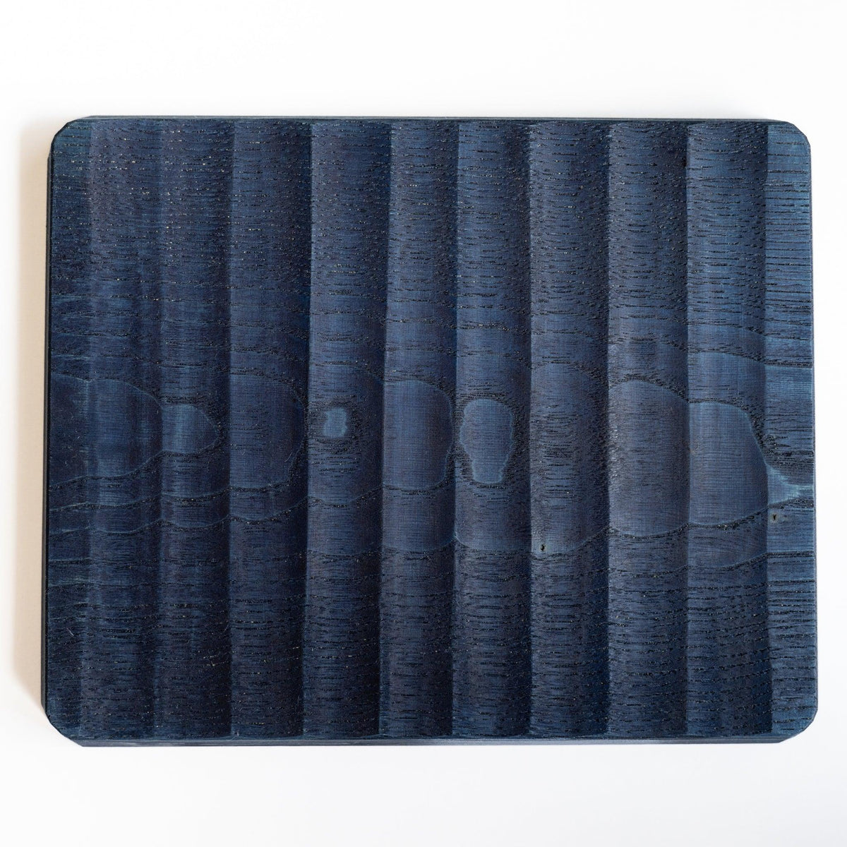 Back of indigo dyed wide chestnut pen tray, broad carved facets across a flat surface with rounded corners