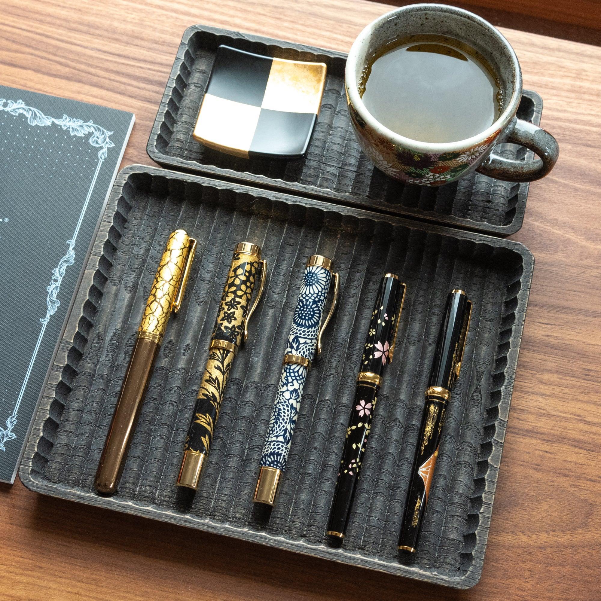 Overhead view of wagatabon wooden pen tray with multiple decorative pens resting in carved slots with clear visibility of