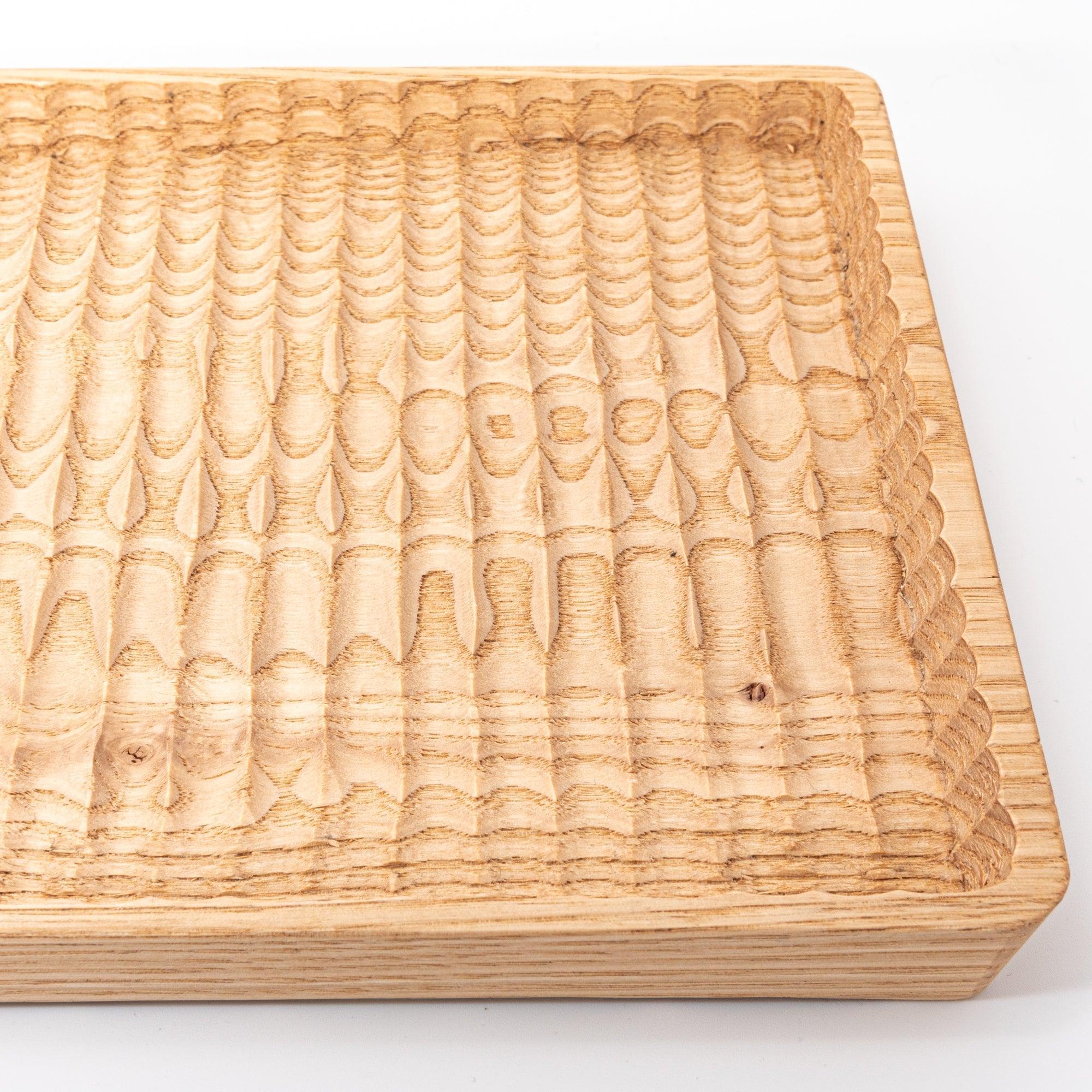 Close-up of a wooden tray showing detailed grooves and a natural wood texture against a white background.