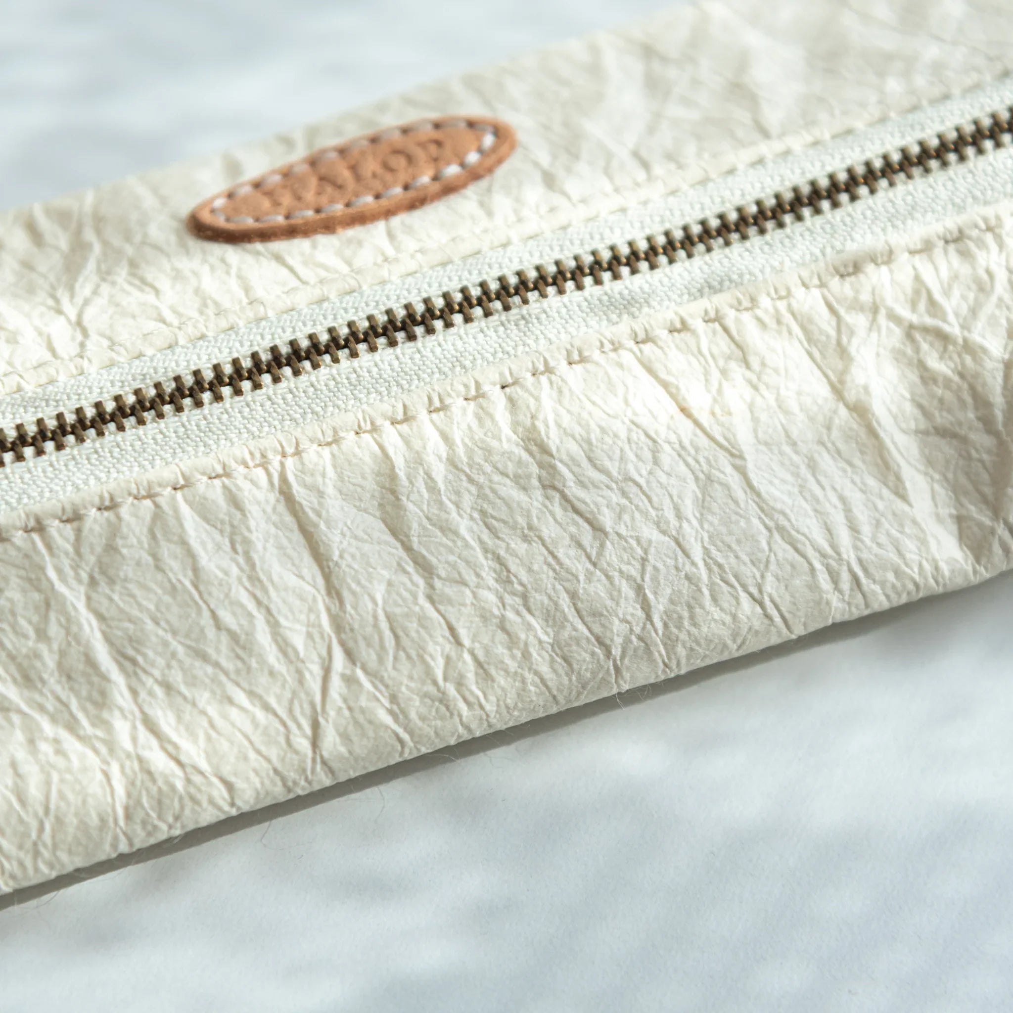 Close-up of the brass zipper and leather ring of the white Japanese Pen Case, showing the washi paper’s soft wrinkles.