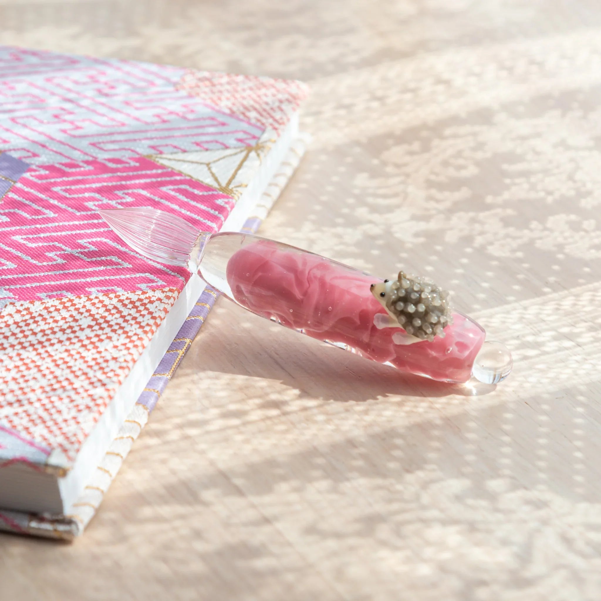 Glass dip pen with whimsical hedgehog design clutching decorative glass ink container with elegance with unique