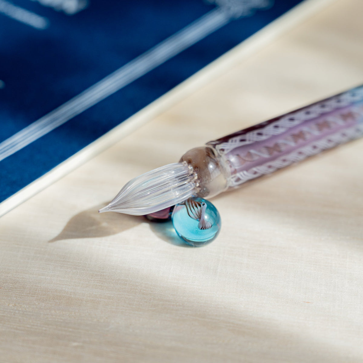 Helix Dawn glass dip pen nib and turquoise sphere pen rest at the corner of a navy blue card