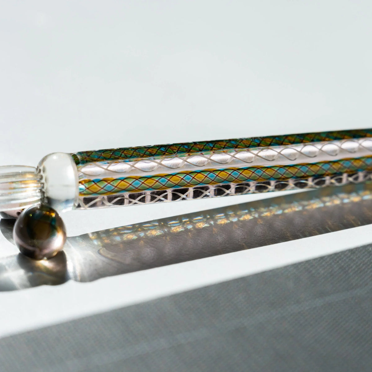 Detail of the Helix Peacock glass canes in teal, gold and white running the length of the barrel