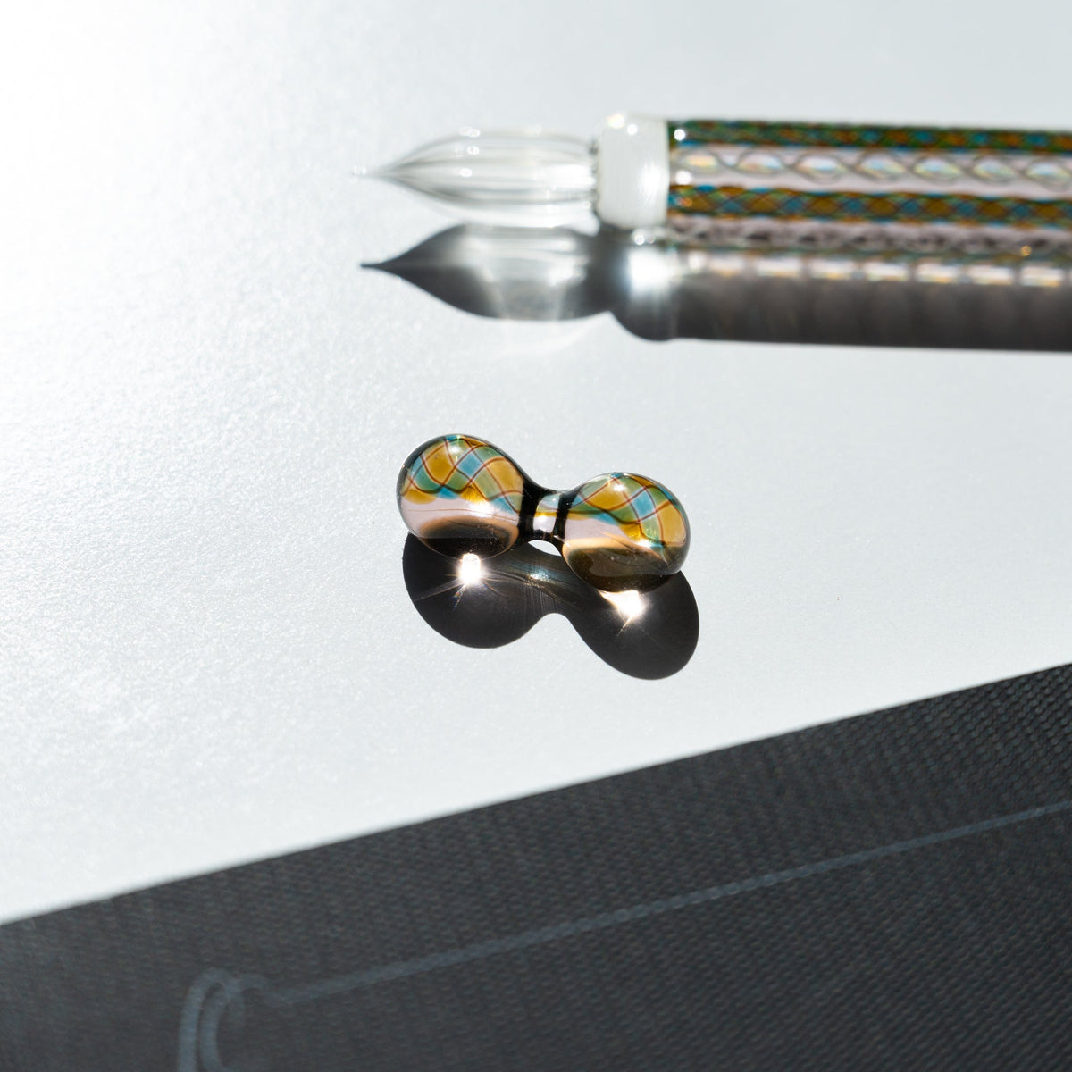 Two-sphere glass pen rest with teal and gold diamond lattice, Helix Peacock pen and nib above