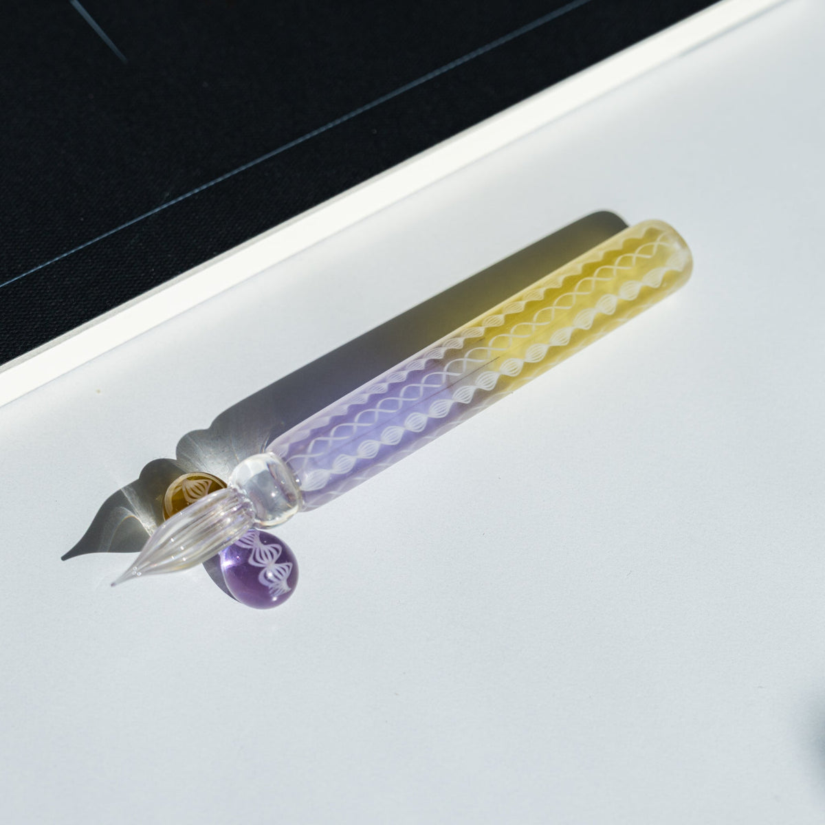 Helix Wisteria glass dip pen, lavender and yellow barrel with white spiral lace canes, on a white tray