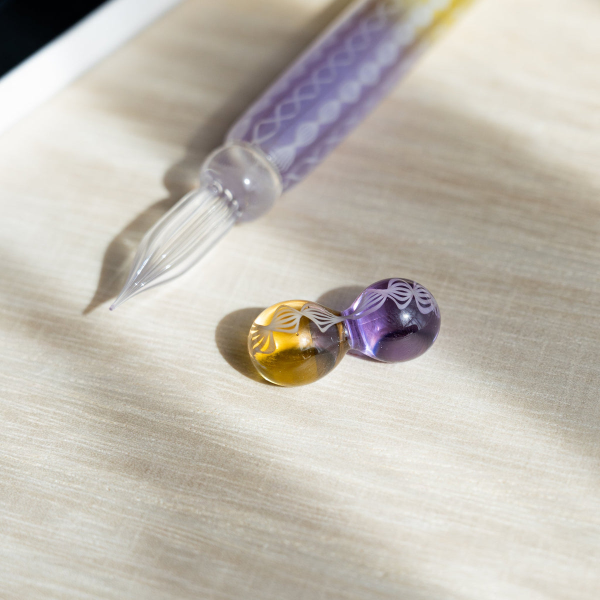 Clear fluted nib of the Helix Wisteria glass dip pen with its amber and lavender glass pen rest in front