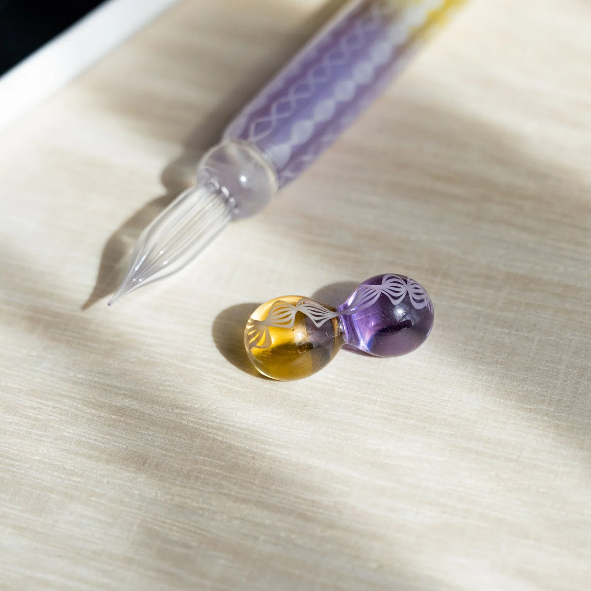 Clear fluted nib of the Helix Wisteria glass dip pen with its amber and lavender glass pen rest in front