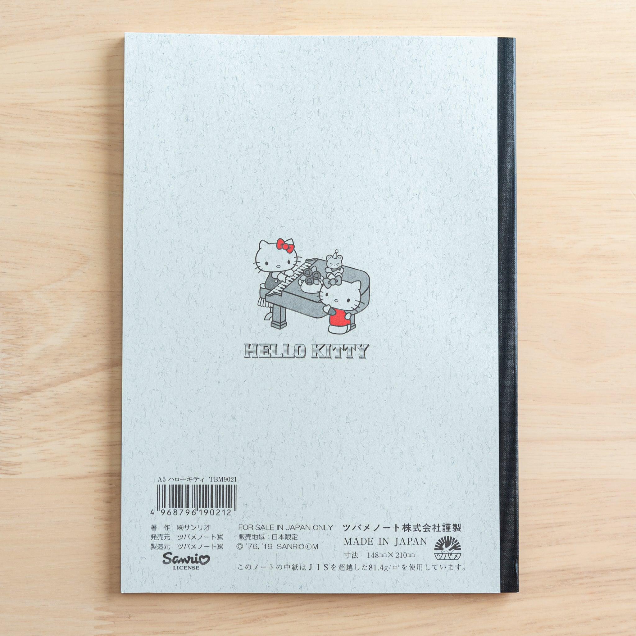 The back cover of a Tsubame Japanese notebook with a Hello Kitty design, featuring a piano illustration, a black spine, product details, and a "Made in Japan" label.