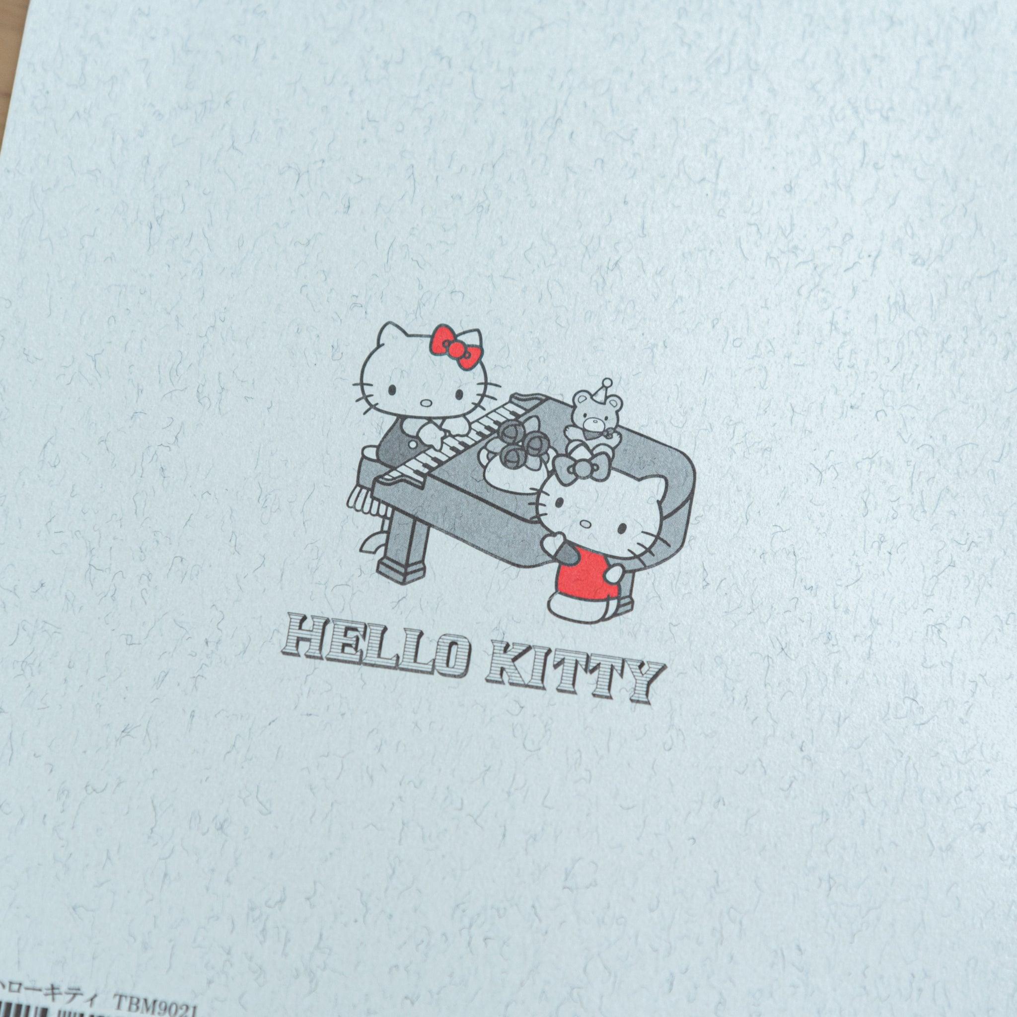 A close-up of the back cover of a Tsubame Japanese notebook, showing a Hello Kitty piano illustration with red accents, combining elegance with playful Japanese stationery.