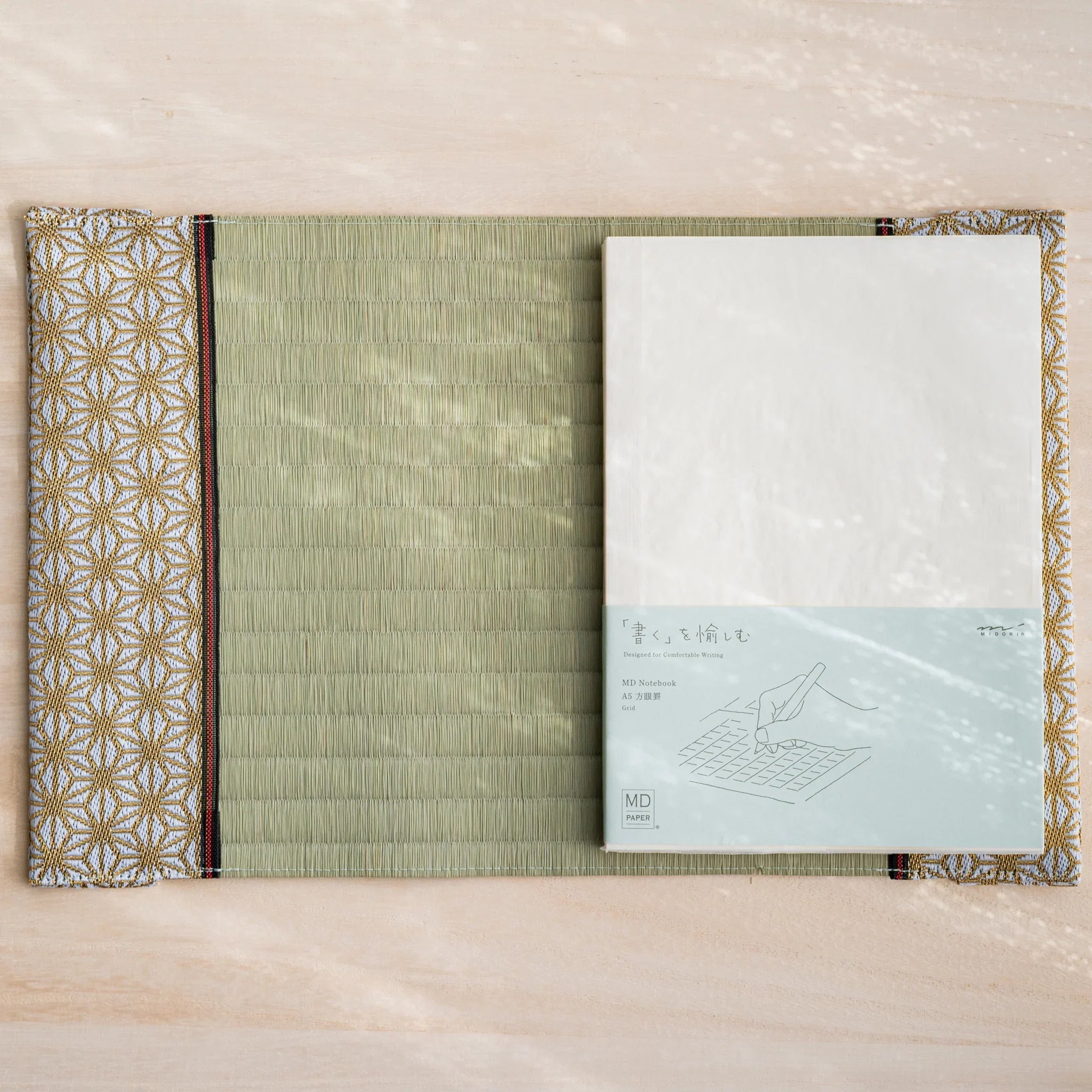 Hemp Leaves tatami book cover open flat with an MD Notebook A5 grid in its paper wrapper on the right side