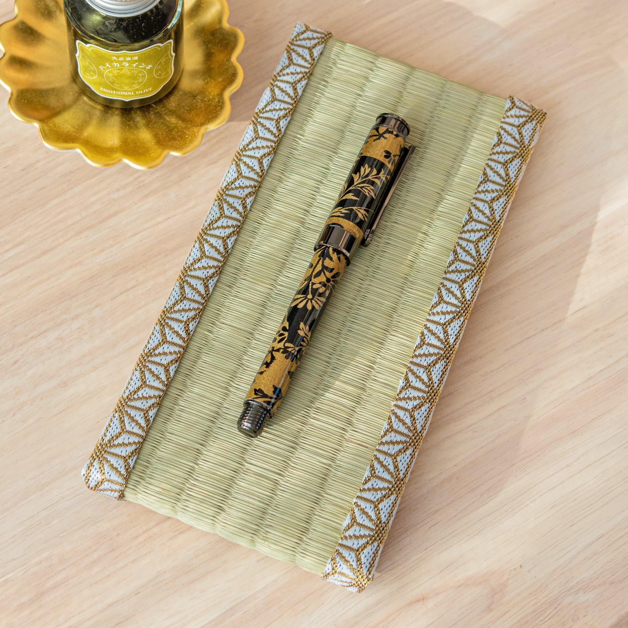A black and gold Japanese stationery fountain pen on a tatami-style pen tray with a golden ink bottle nearby.