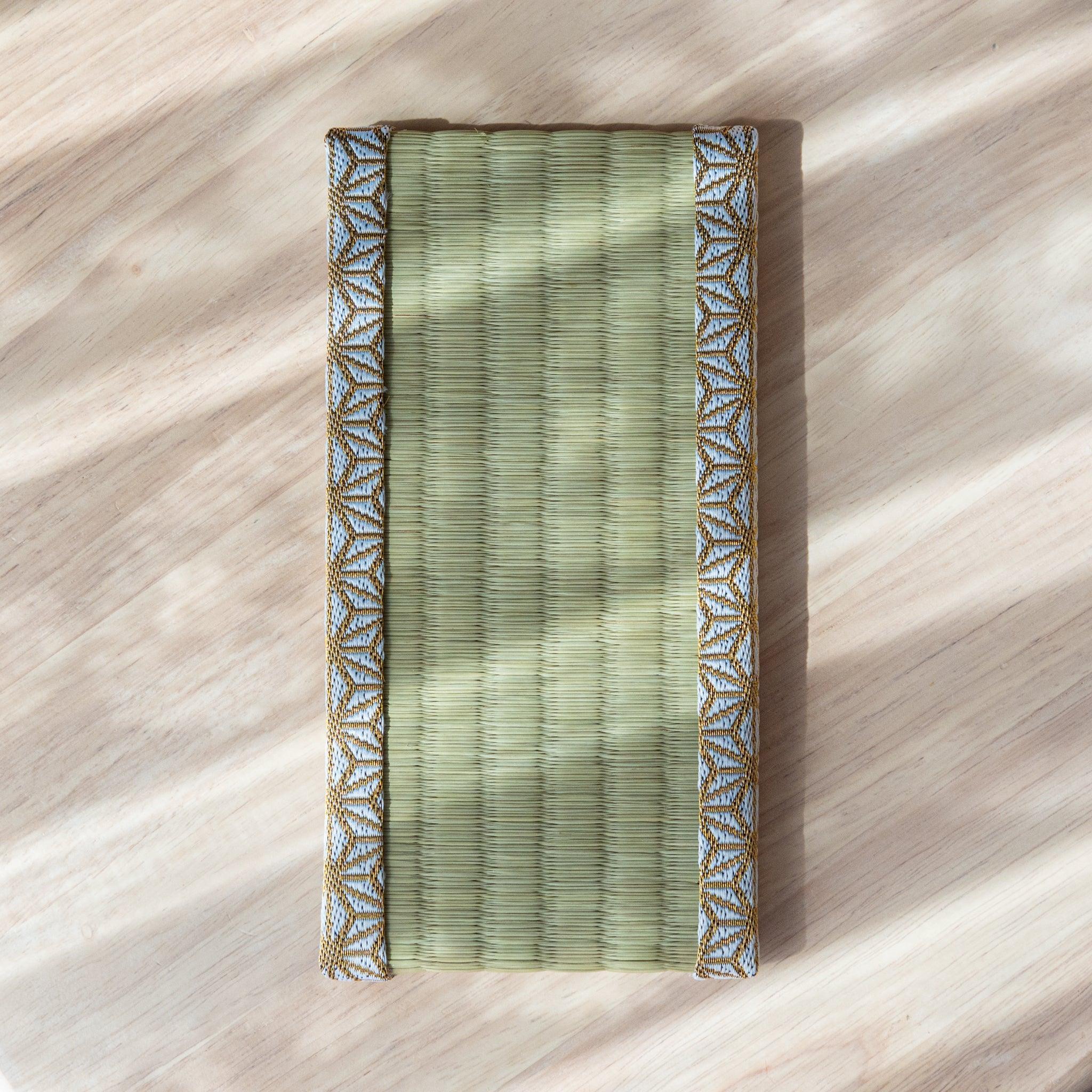 A tatami-style pen tray with gold and white trim placed on a wooden surface under natural light.
