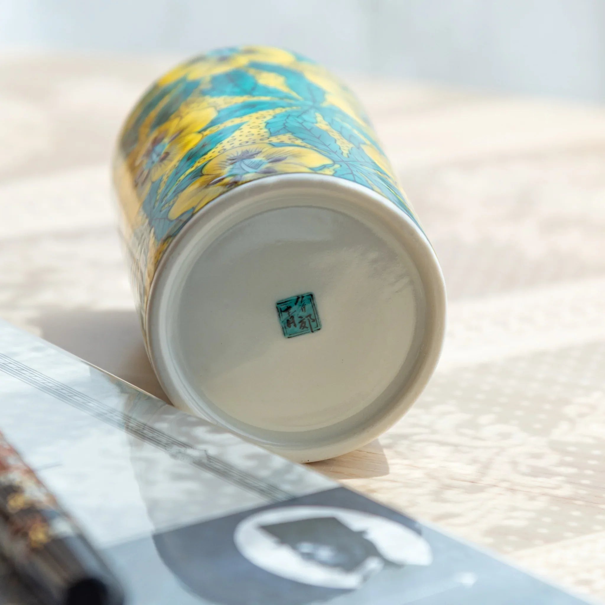 Kutani ceramic pen holder tipped showing unglazed base with teal square maker's seal and yellow hollyhock floral exterior