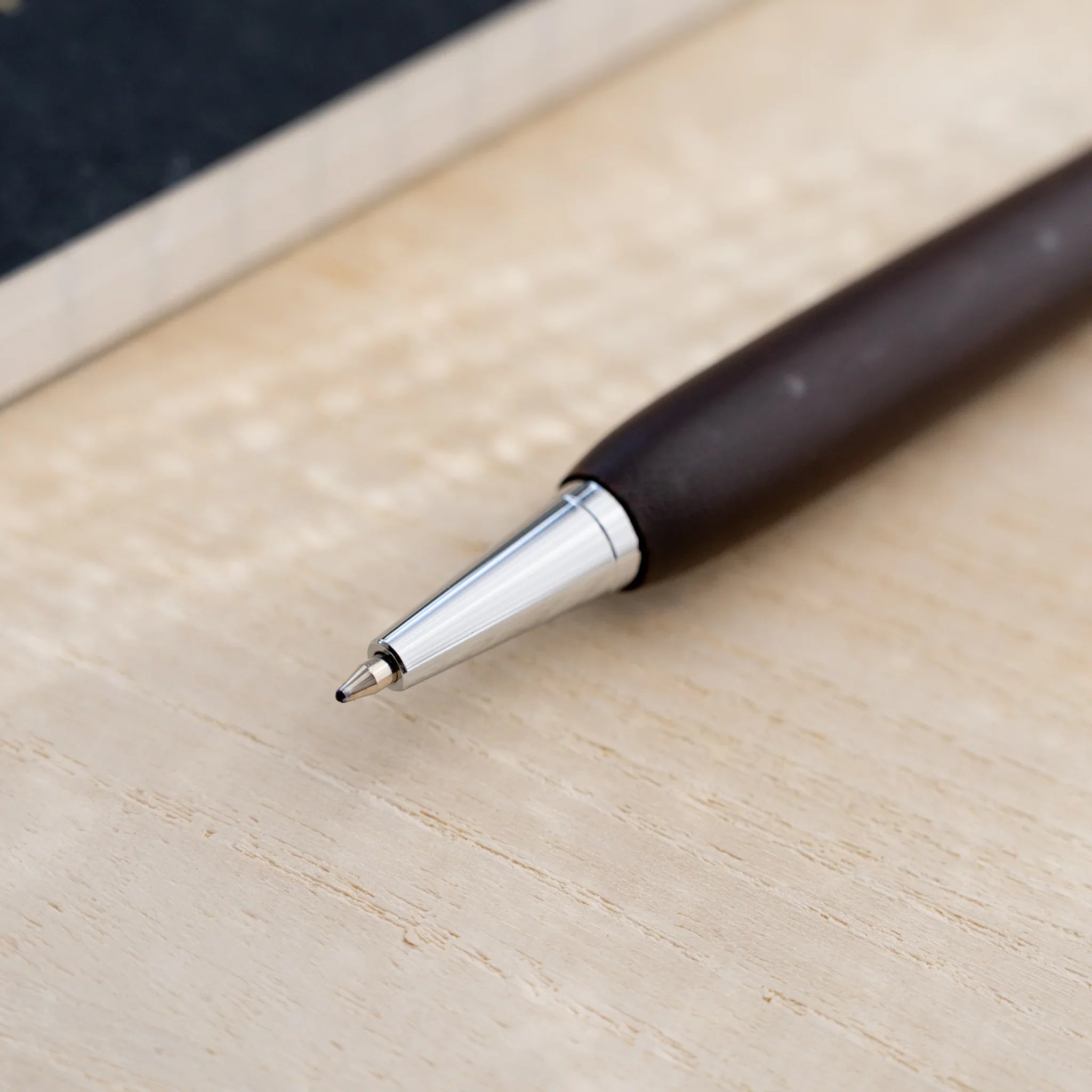 Chocolate brown horse chestnut wood urushi ballpoint pen, close-up of lower barrel and silver cone tip, Japanese wood