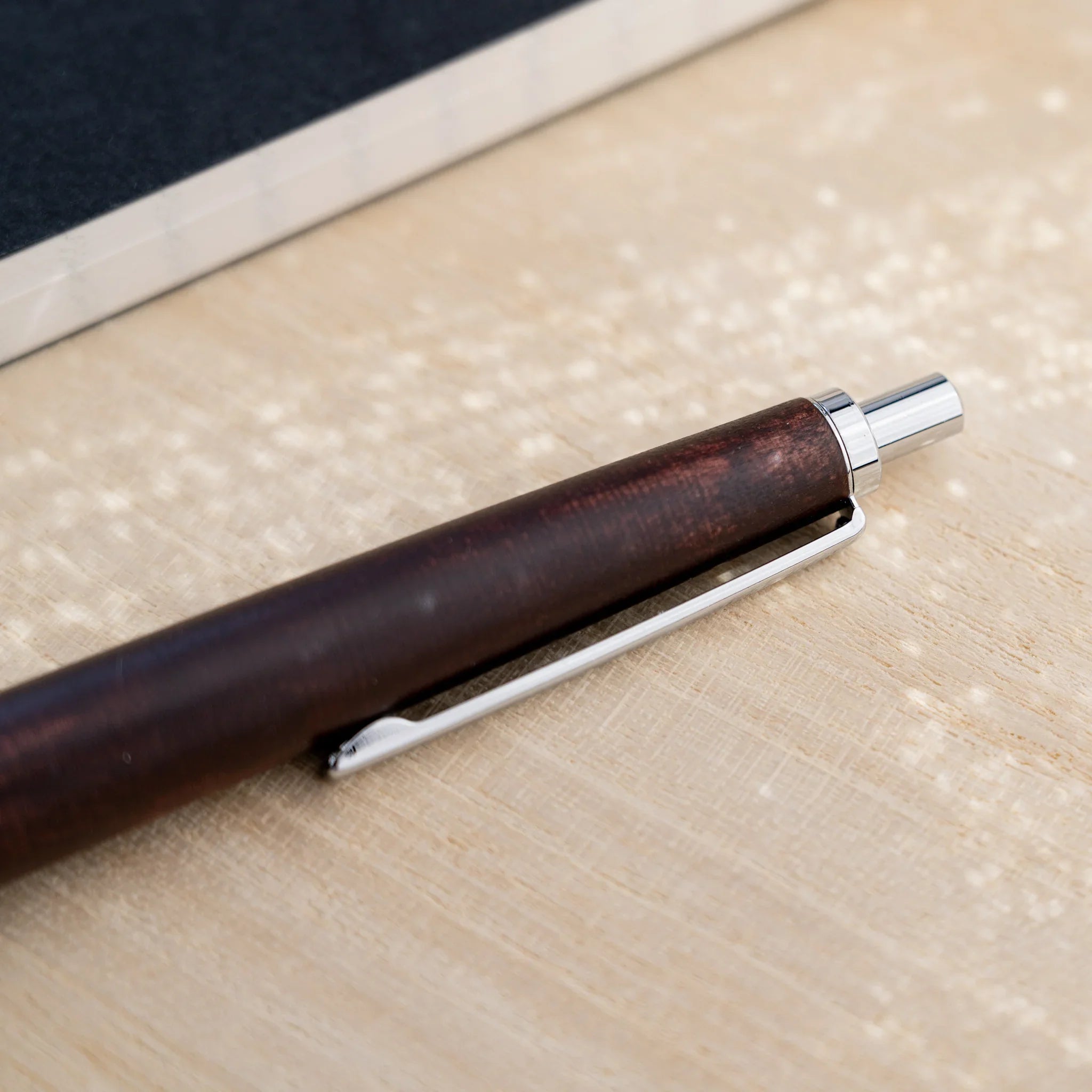 Chocolate brown horse chestnut wood urushi ballpoint pen, close-up of barrel and silver knock end, Japanese wood